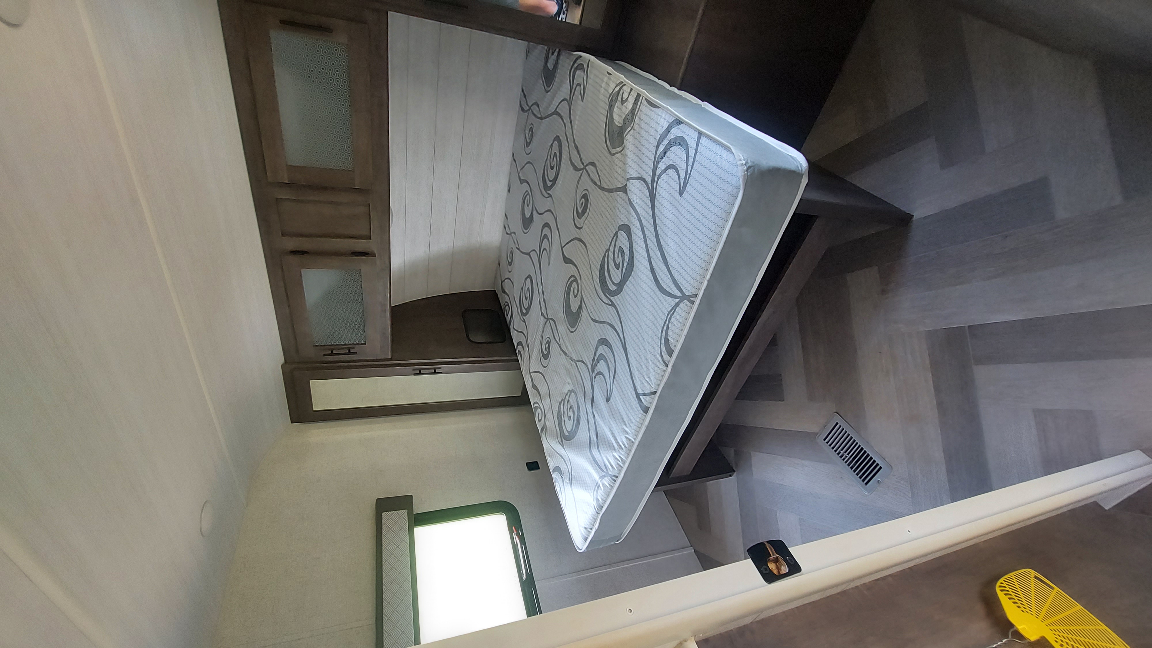 RV rental bedroom: cozy space featuring a patterned mattress on a raised platform, wood cabinets, and herringbone flooring.. Forest River Wildwood 2020