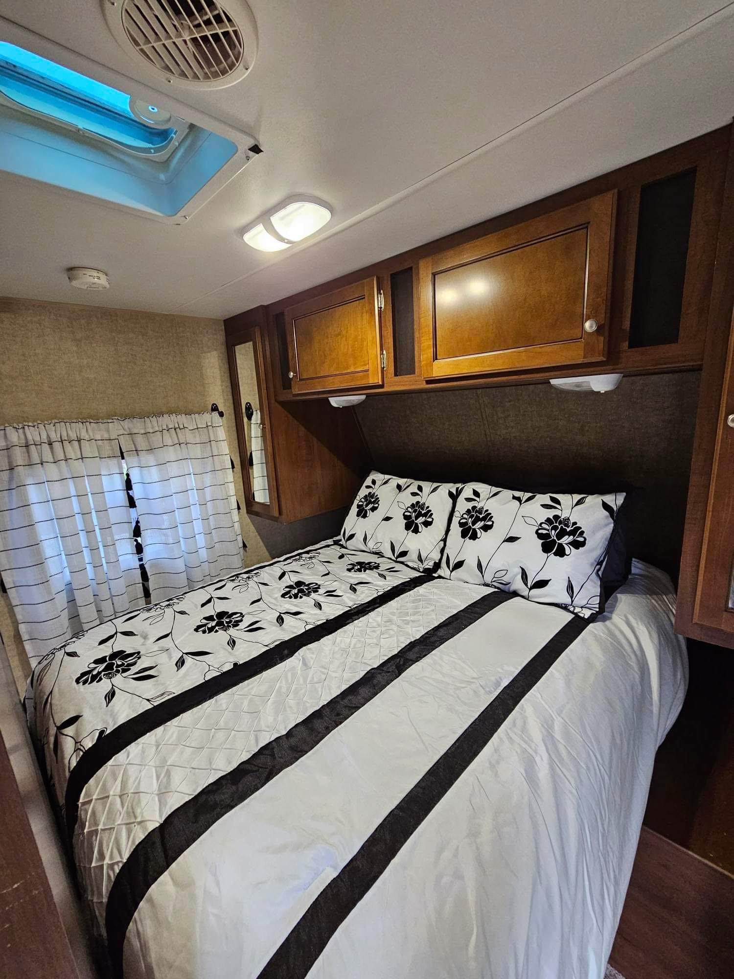 Cozy RV bedroom with black & white floral bedding, overhead storage, skylight, and AC. Ideal for your RV rental adventure.. Heartland Prowler 2015