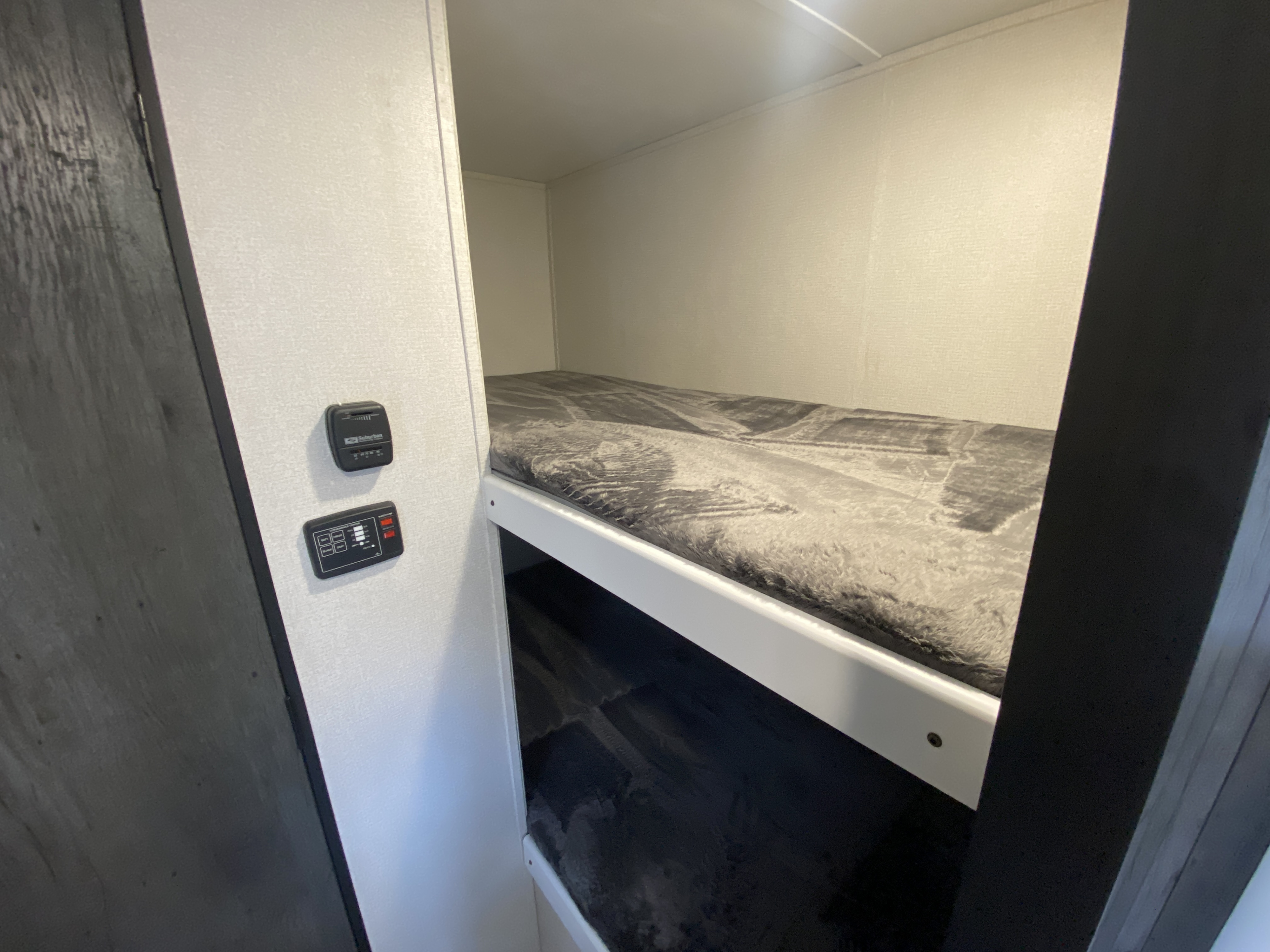 Inside an RV rental: a compact sleeping area with bunk beds. The upper bunk has a soft, grey blanket, and wall controls are visible.. Keystone Hideout 2022