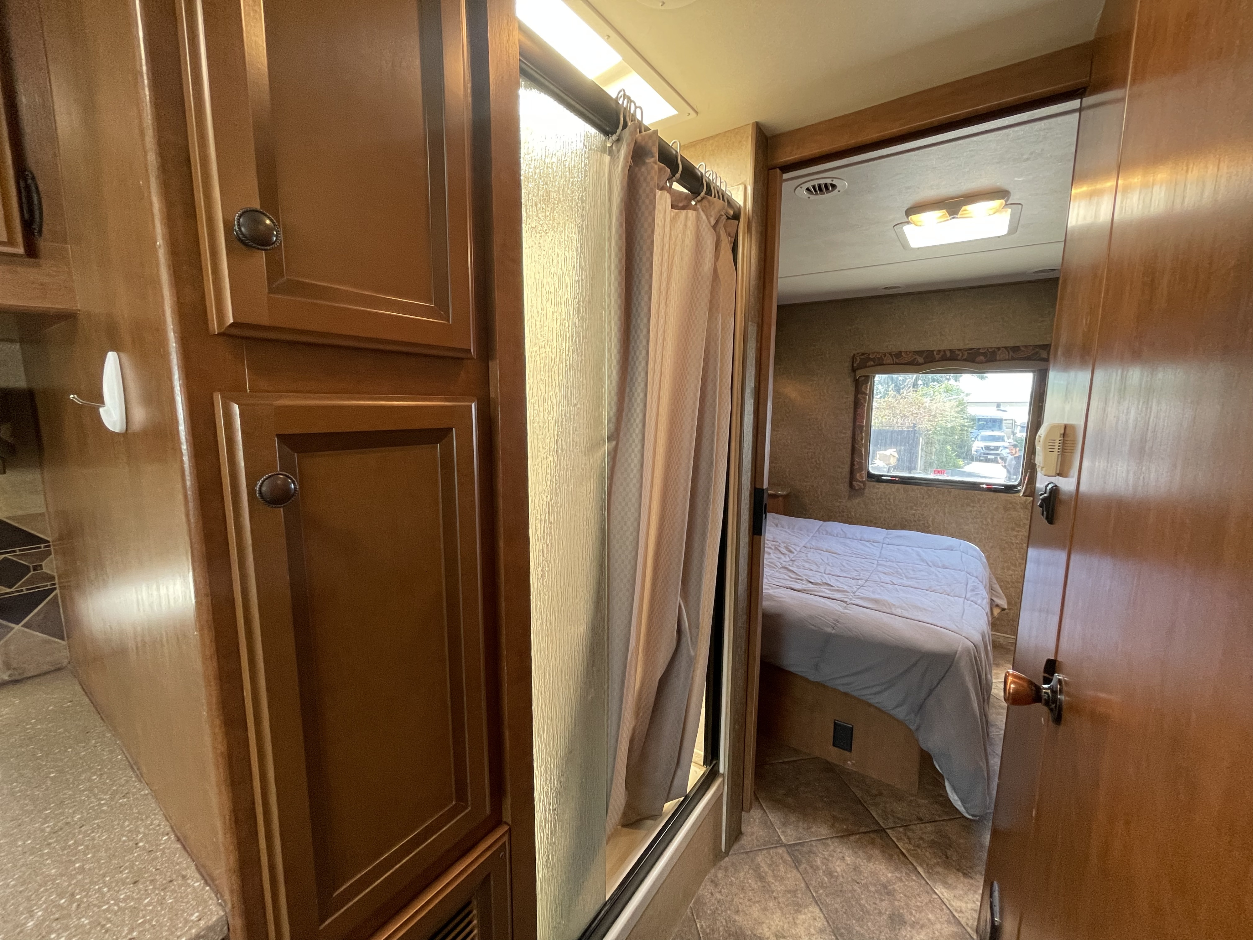 RV rental's inviting interior: view of the shower area, wood cabinets, and a cozy bedroom with natural light. Ideal for travel.. Thor Motor Coach Windsport 2014