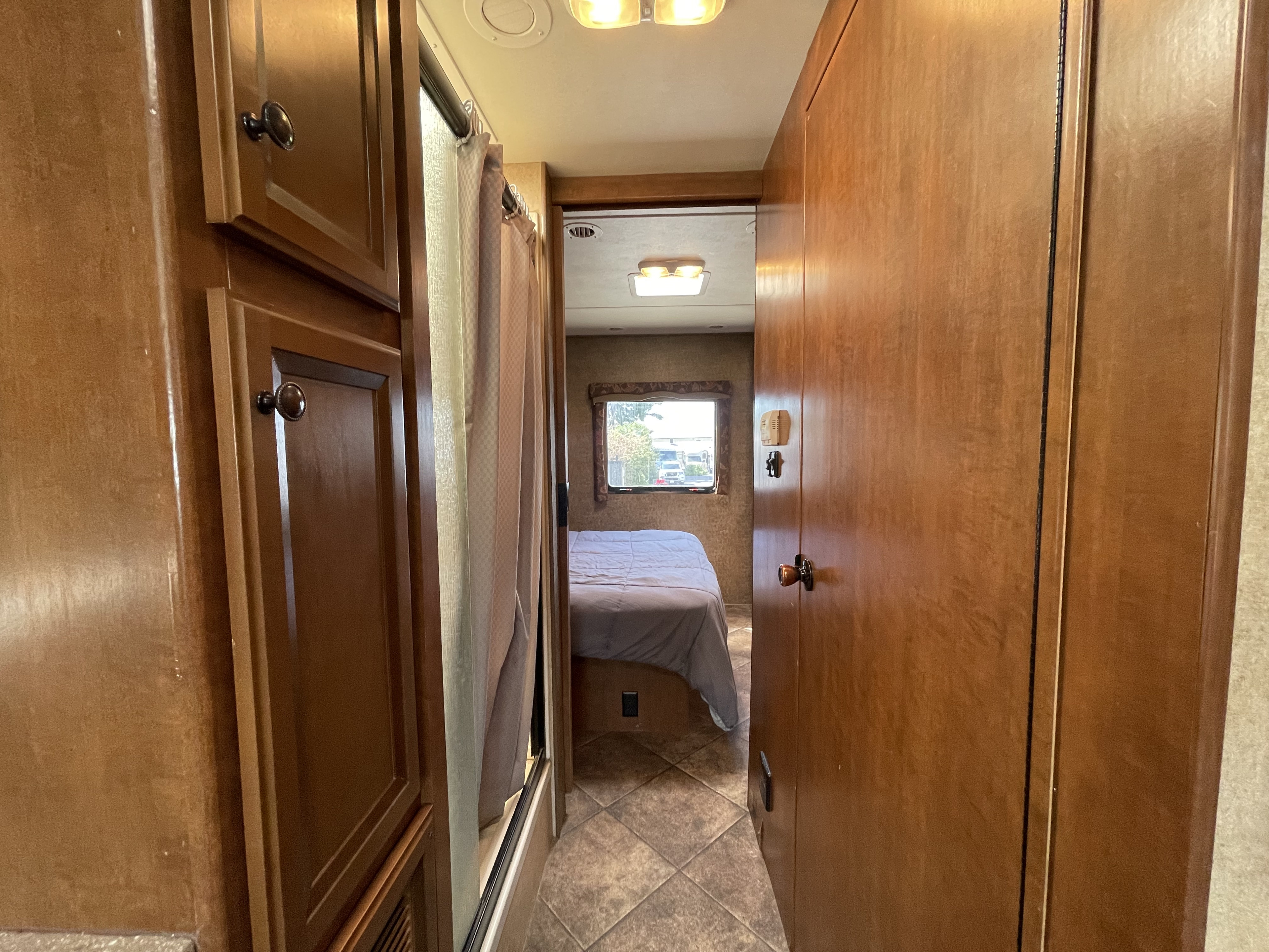 RV rental interior: View down a hallway into a bedroom with a bed, window, and built-in wood cabinetry.. Thor Motor Coach Windsport 2014