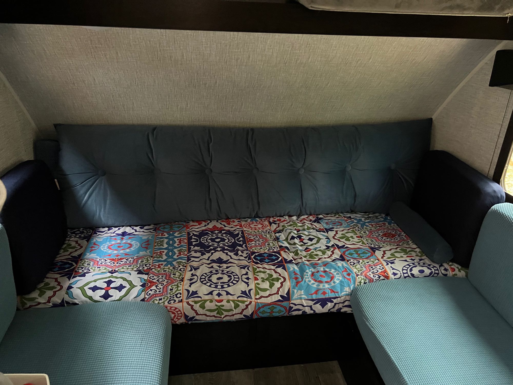 Cozy RV rental interior featuring a blue tufted sofa bed and colorful patterned bedding, with light blue seating in the foreground.. Braxton Creek Bushwhacker Plus 2022