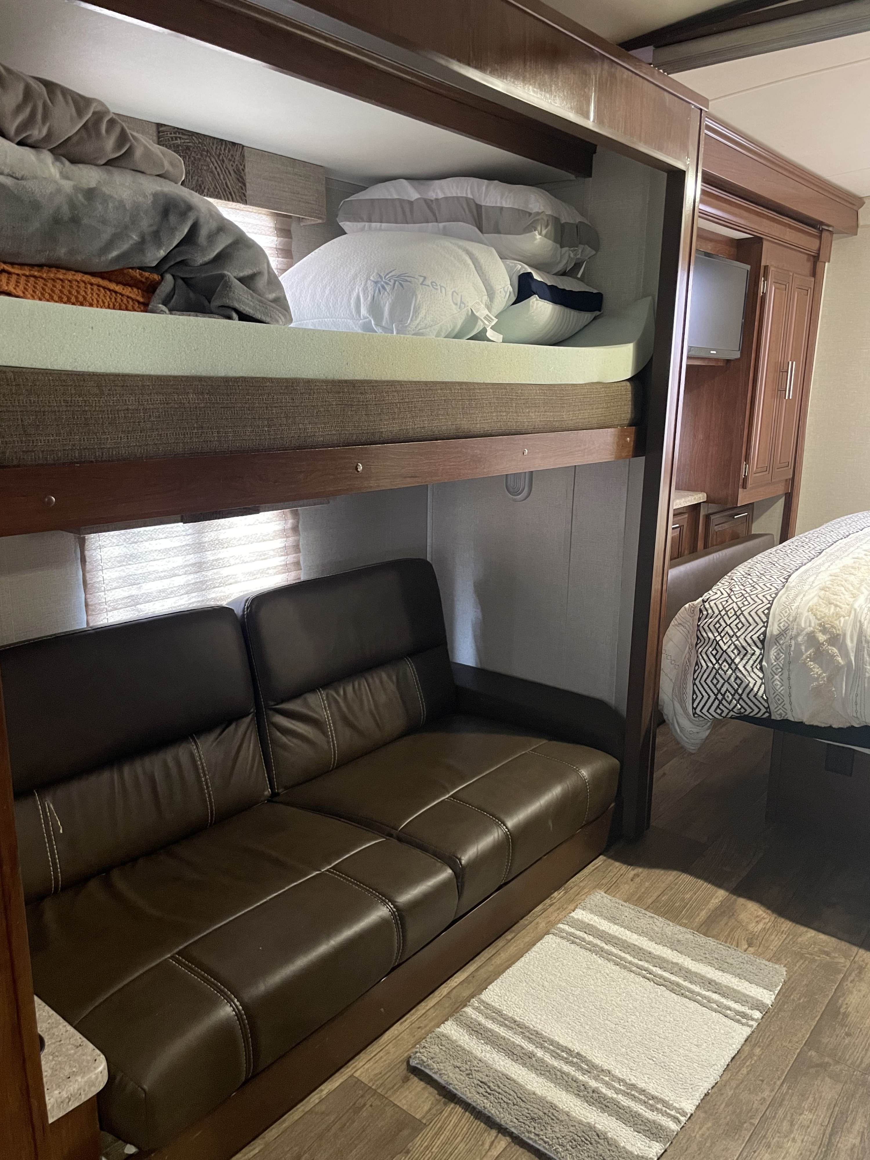 RV rental interior: bunk beds with pillows, brown leather sofa, and main bed with patterned comforter.. FR3 FR3 Motorhome 2018