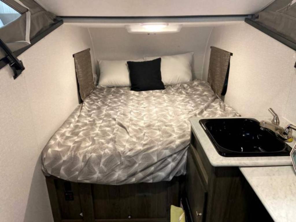 Compact RV rental interior featuring a cozy bed with patterned bedding, pillows, and a small sink/kitchenette area.. Coachmen Clipper 2022
