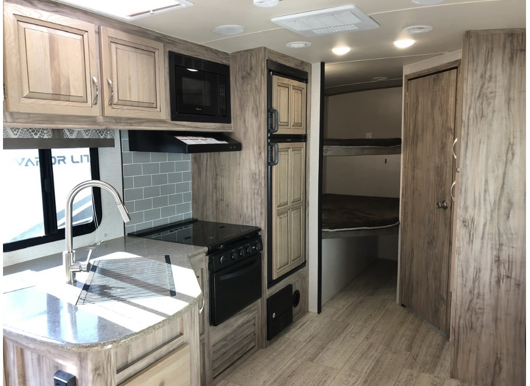 Inside an RV rental: full kitchen with sink, microwave, stove, fridge, and bunk beds for extra sleeping space.. Palomino 240bhs 2018