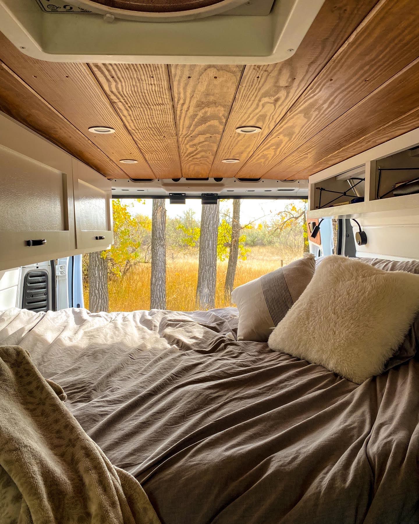 Cozy RV rental interior: a comfortable bed with neutral bedding, wooden ceiling, and a scenic autumn view outside.. Other Other 2019
