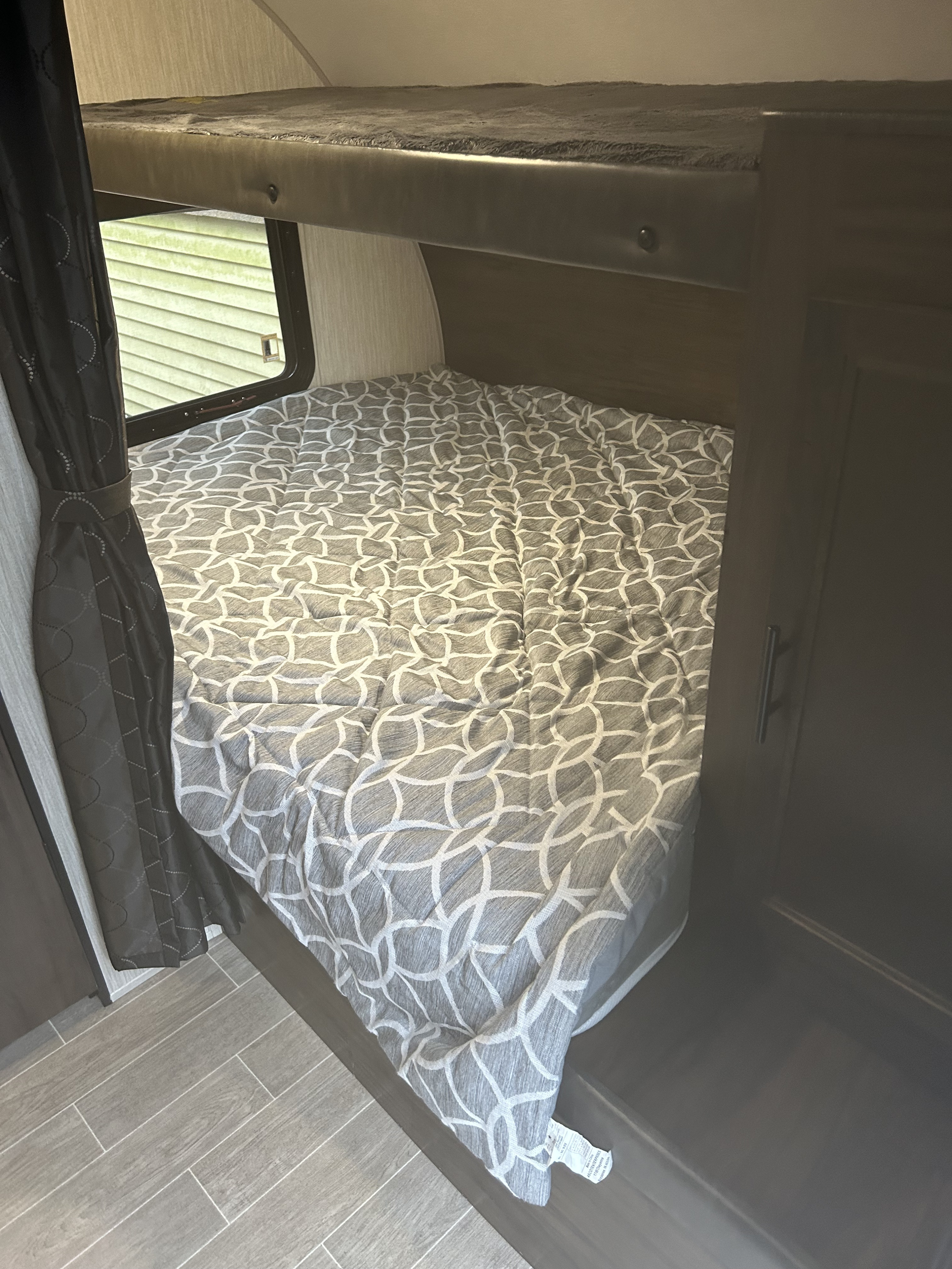Interior of RV rental showing bunk beds: a lower bed with grey patterned bedding, an upper bunk, and a window to green siding.. Forest River Cherokee Grey Wolf 19SM 2021