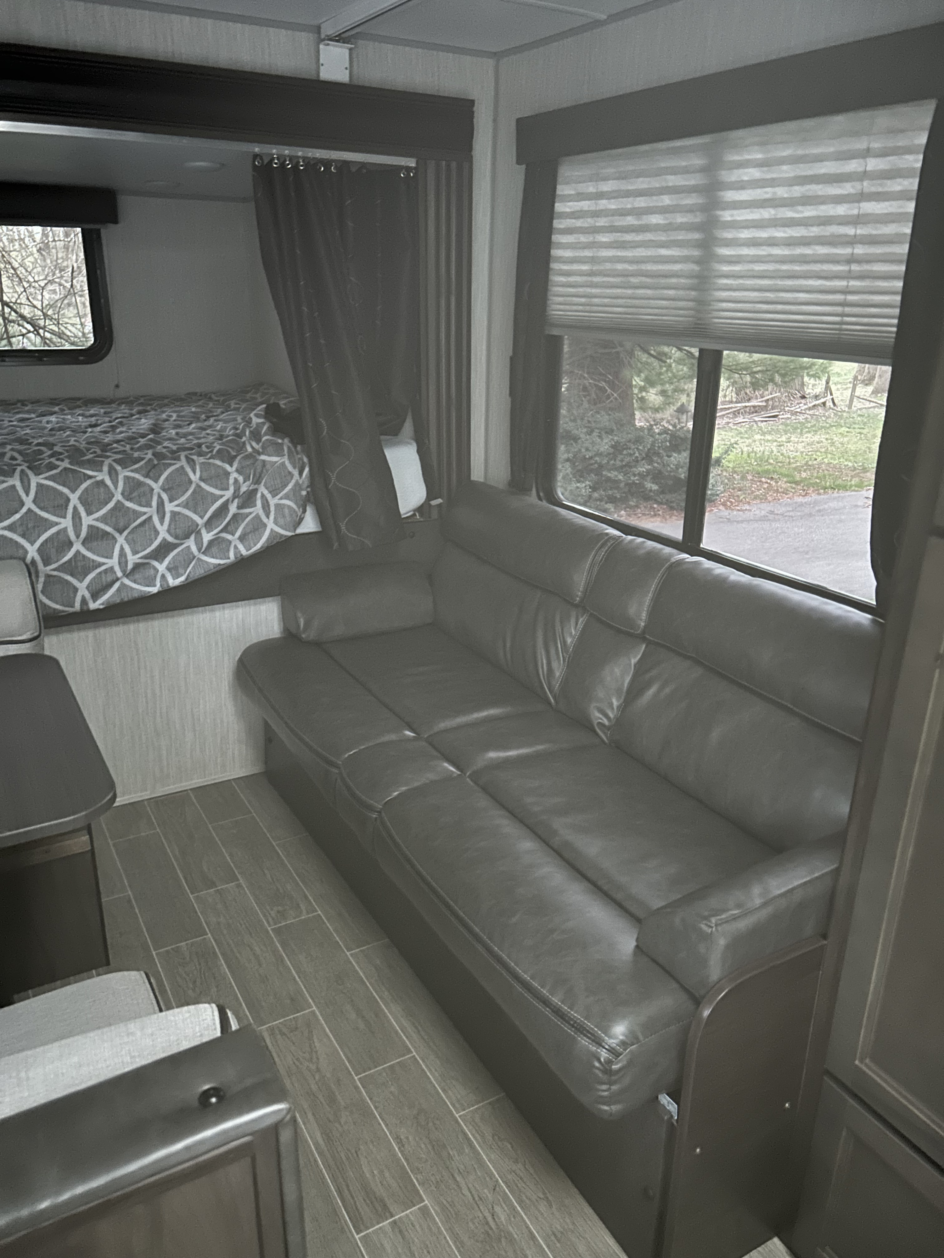 Step inside this modern RV rental featuring a comfortable bed, large gray sofa, and scenic window views over wood-look flooring.. Forest River Cherokee Grey Wolf 19SM 2021
