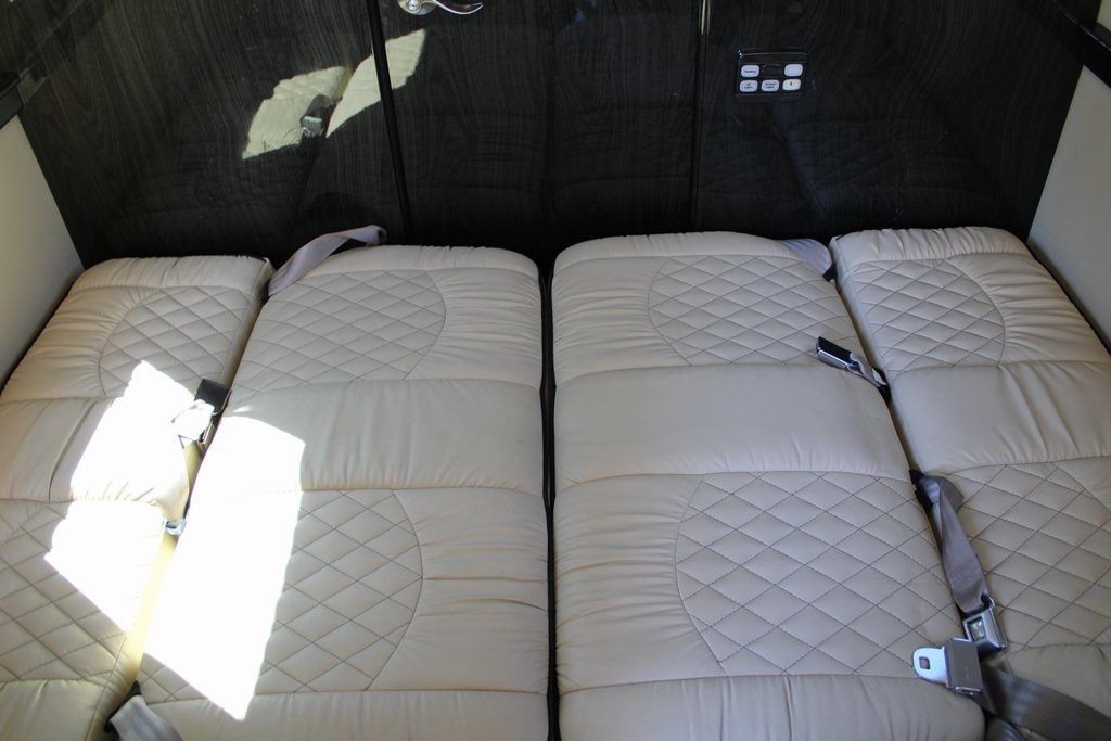 Comfortable cream quilted beds with seatbelts in an RV rental interior, ready for travel or rest. Sunlit detail.. Midwest Automotive Designs Ultimate Presidential 2021