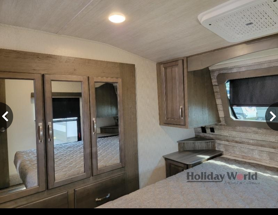 Spacious RV rental bedroom featuring a comfy bed, mirrored closet, overhead cabinets, and built-in nightstands.. Keystone Cougar 2023