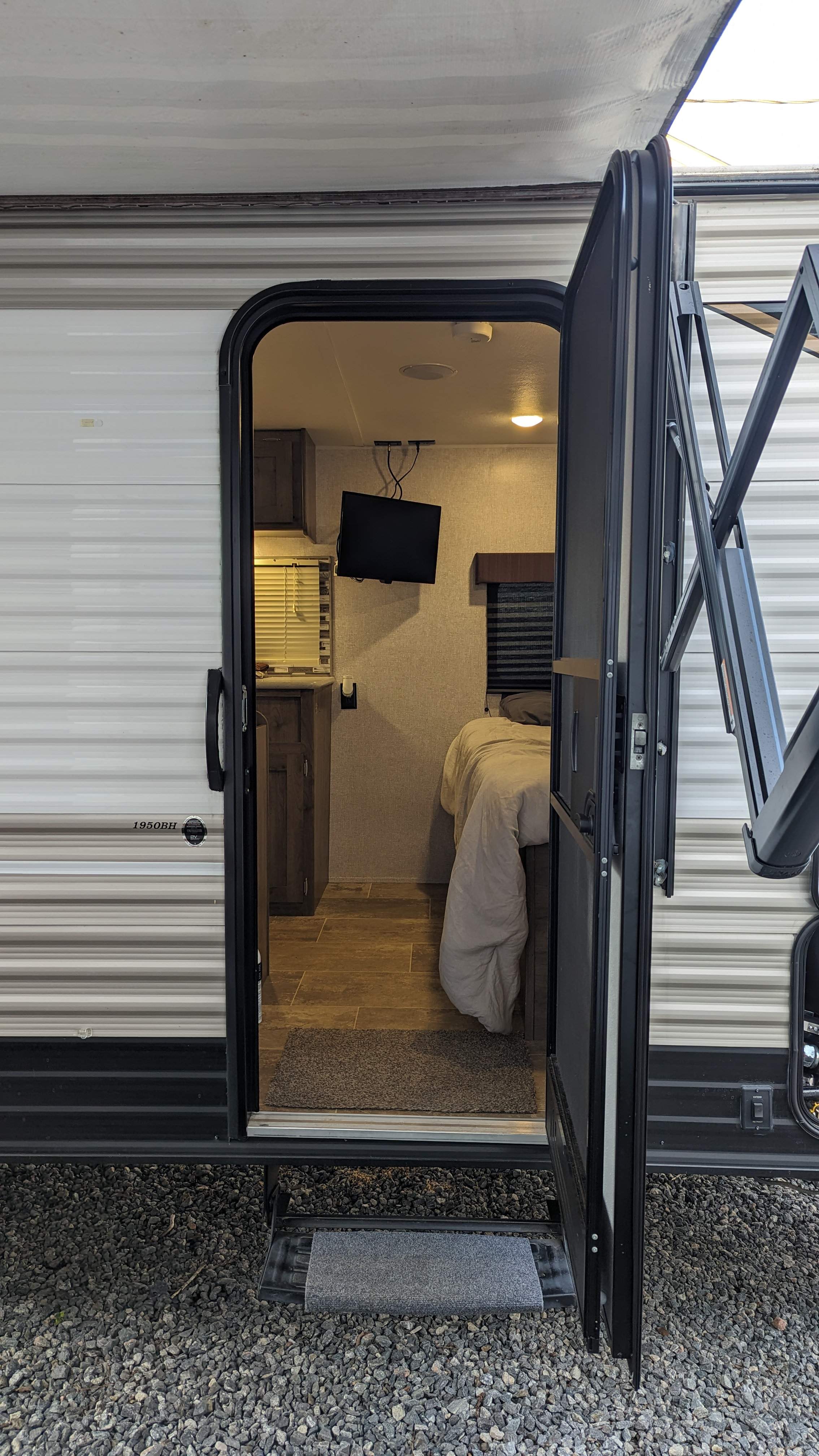 Step inside this cozy RV rental! View of the interior from the open door, revealing a bed, TV, and kitchen area. Perfect for travel adventures.. Aspen Trail LE 2020