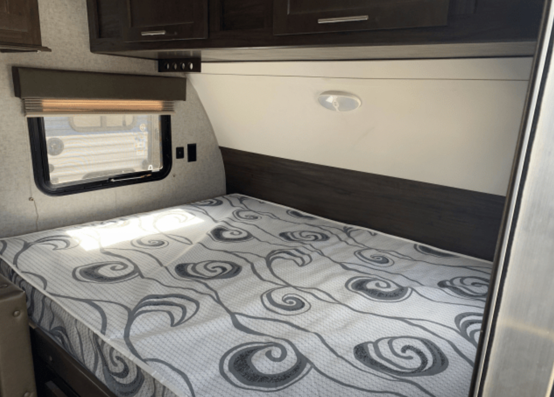 Inside an RV rental: a cozy bedroom features a patterned mattress, window, and dark wood cabinets. Ready for adventure.. Forest River Cherokee Wolf Pup 2019
