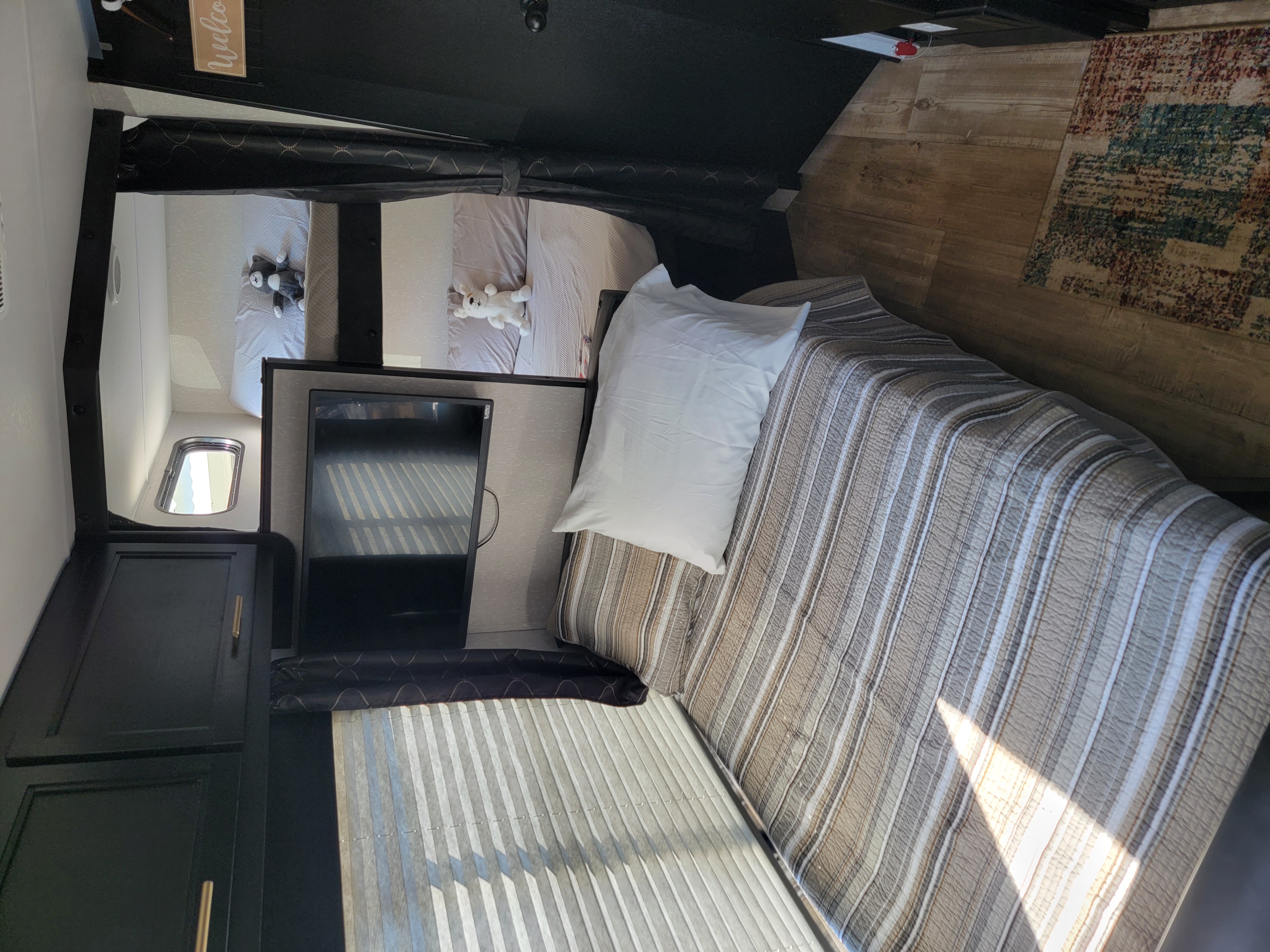 Cozy RV rental interior with main bed, bunk beds & plush toys, modern black cabinets, and wood-look floor.. Forest River Cherokee Grey Wolf 2022