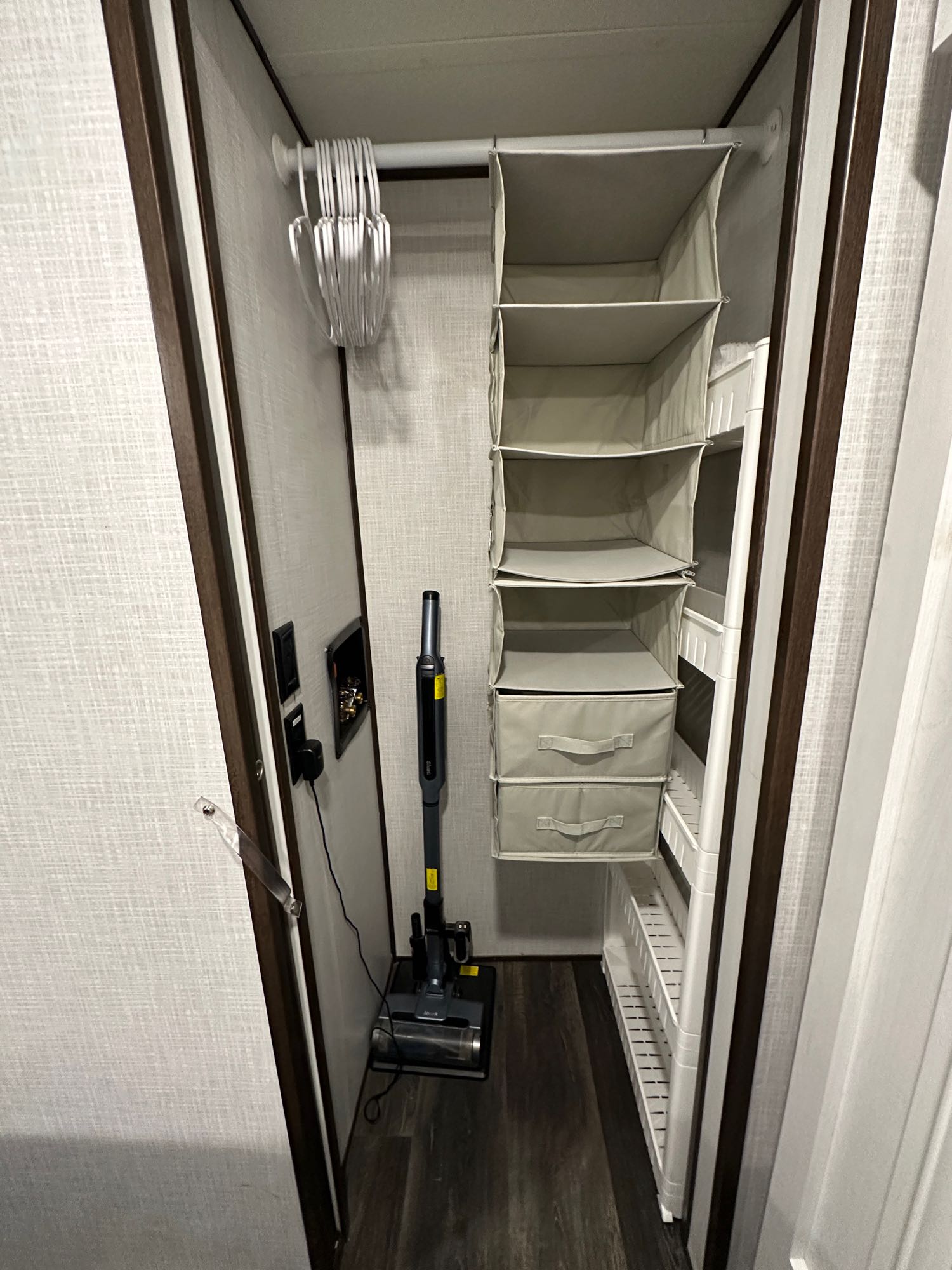 RV rental organized closet: overhead rod with hangers, hanging fabric storage, narrow shelving unit, and a stick vacuum.. Dutchmen Atlas 2022