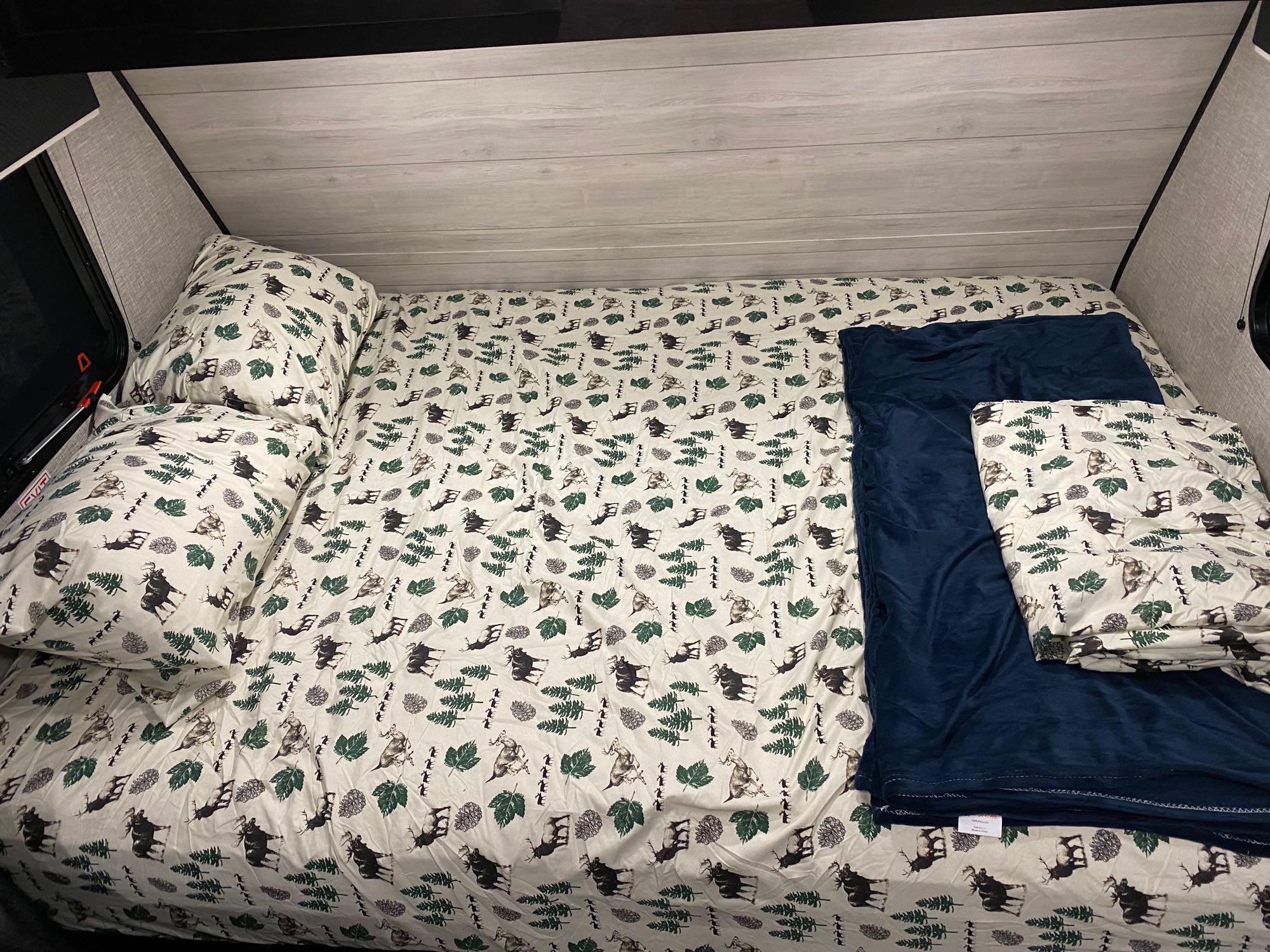 Cozy RV rental bed with nature-themed sheets (moose, leaves) and blue blanket, perfect for camping adventures.. Jayco Jay Flight SLX 2022