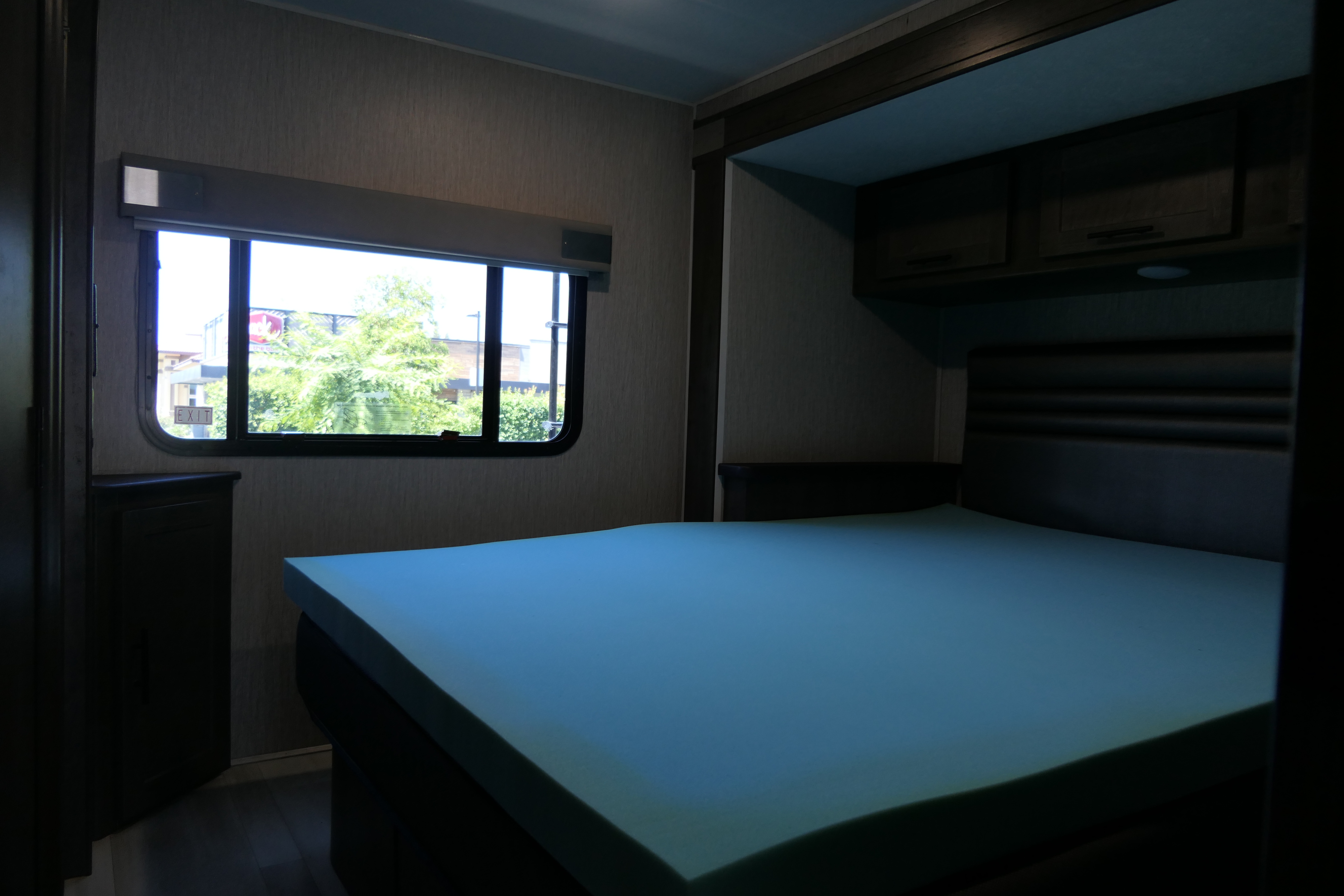 RV rental bedroom with light blue foam bed, window view, and storage. Ideal for travel accommodation.. Coachmen Leprechaun 2021