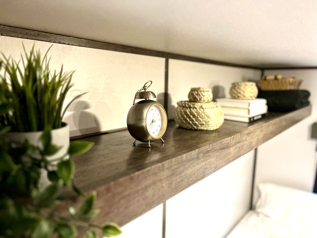 Cozy RV rental interior: A wooden shelf holds a clock, woven baskets, books & a plant, offering organized comfort.. Riverside RV Retro 165 2022