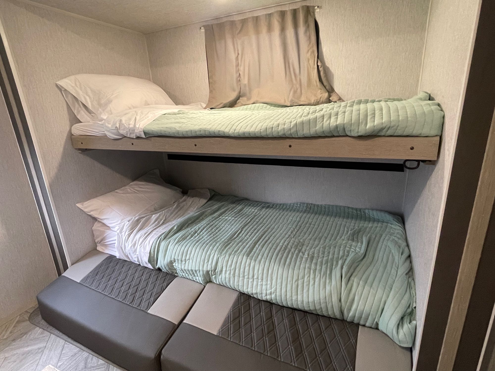 Compact RV rental interior featuring two comfortable bunk beds with light green comforters and convertible seating below.. Forest River Wildwood 32BHDS Platinum 2023