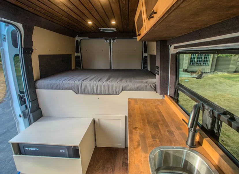 Inside this RV rental: a built-in bed, Dometic fridge, and wood kitchen counter. Ideal camper van setup.. Dodge Ram 1500 2021