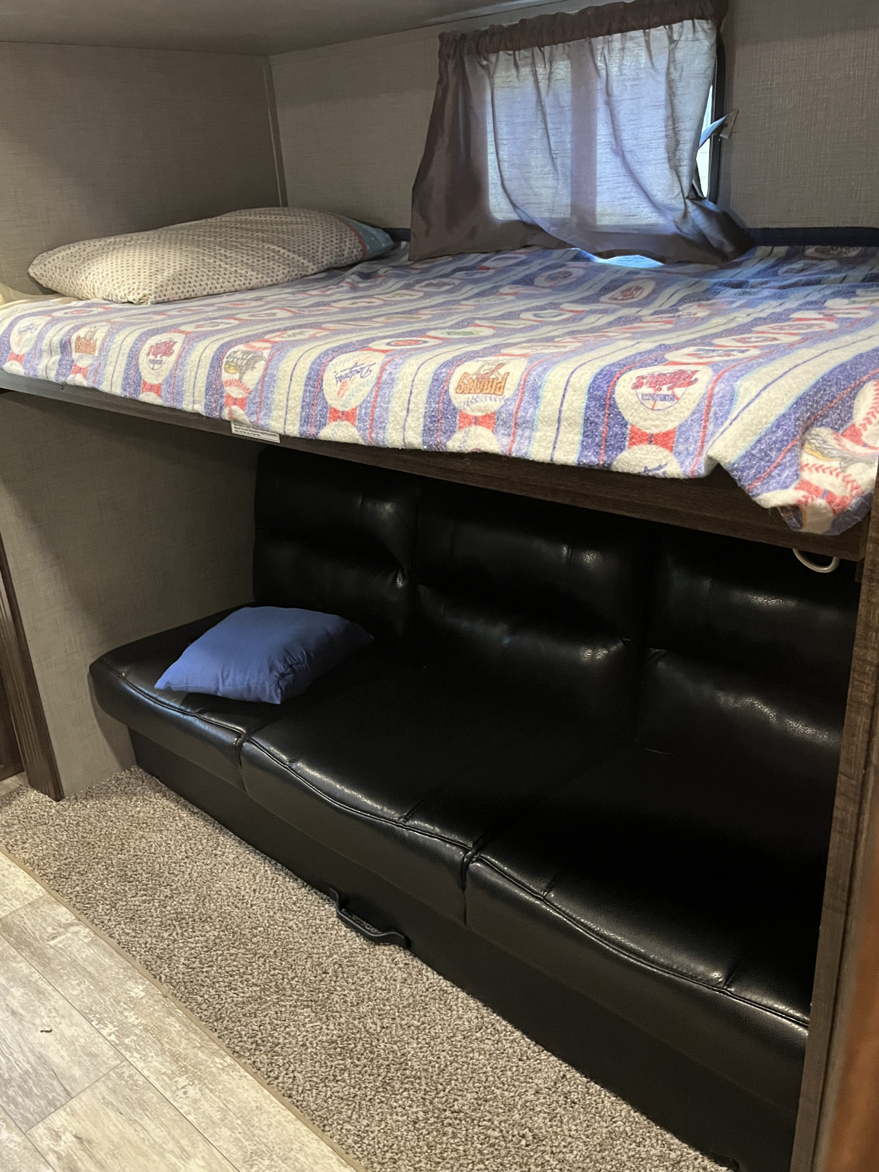 RV rental bunk beds feature a vibrant patterned blanket, a comfortable lower futon, and a blue pillow, perfect for compact sleeping.. Crossroads RV Zinger 2019
