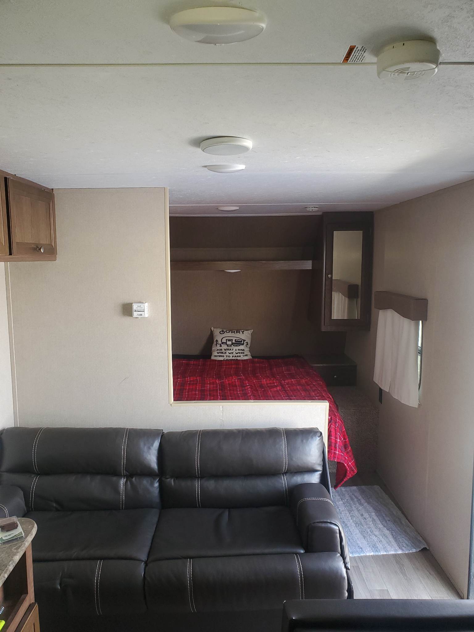 Cozy RV rental interior: black sofa, compact bedroom with red plaid bedding, and ceiling lights.. Dutchmen Coleman Lantern 2016