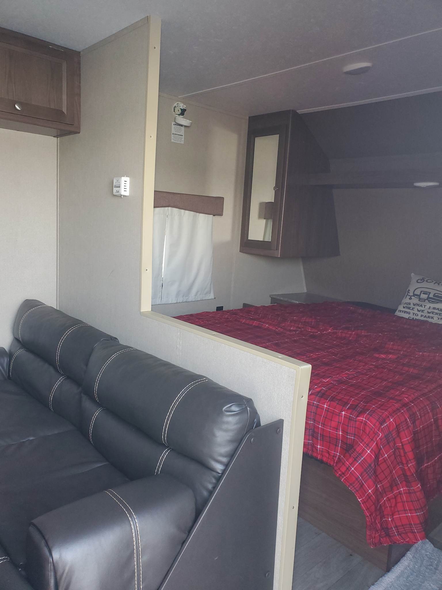 Cozy RV rental interior showing a black sofa, partition wall, and a bedroom with a red plaid bed. Perfect for your next camper adventure.. Dutchmen Coleman Lantern 2016