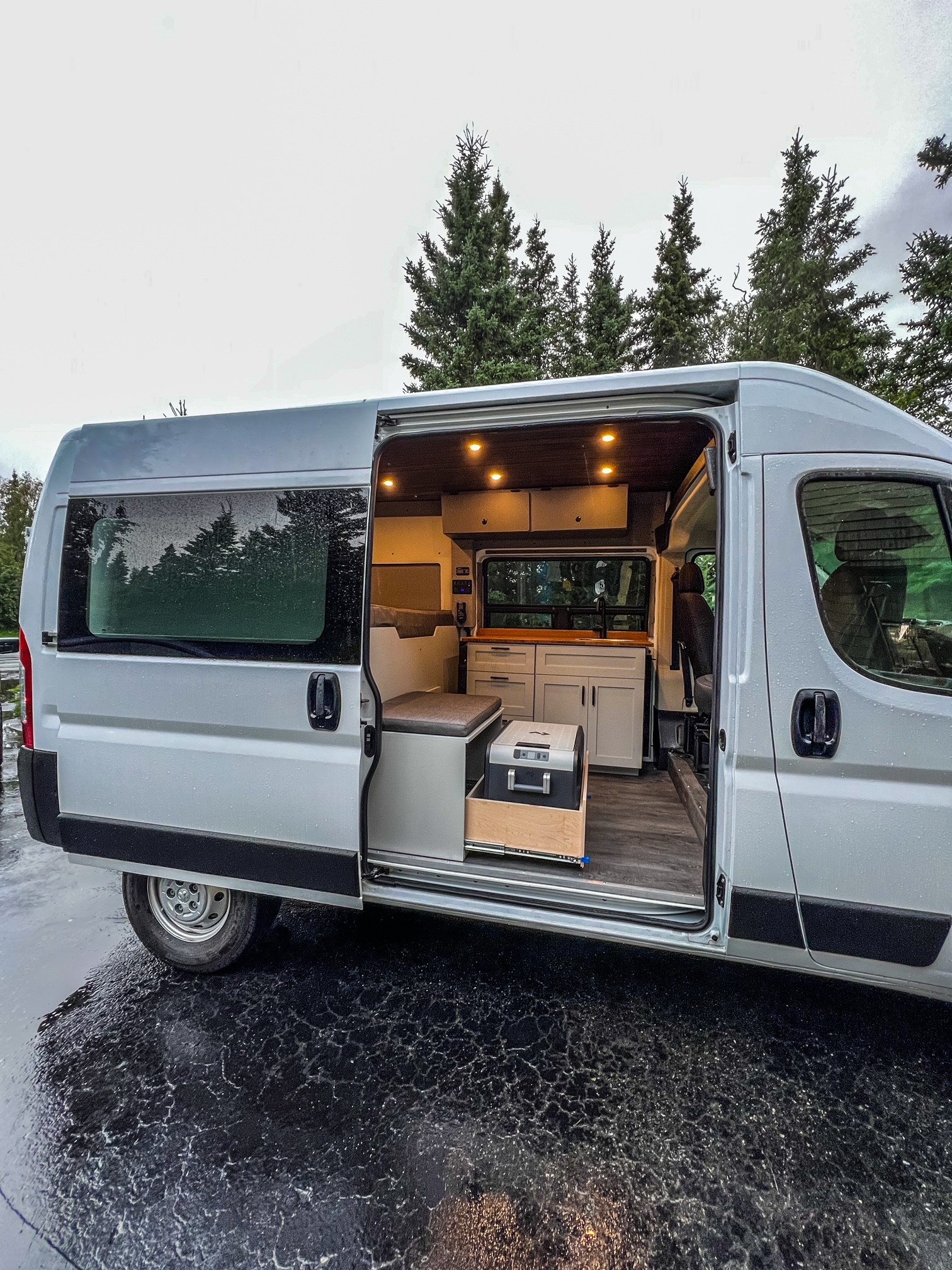 Step inside this custom RV rental, a modern camper van conversion with a cozy interior kitchen & seating area on a wet day.. Dodge Ram 1500 2021