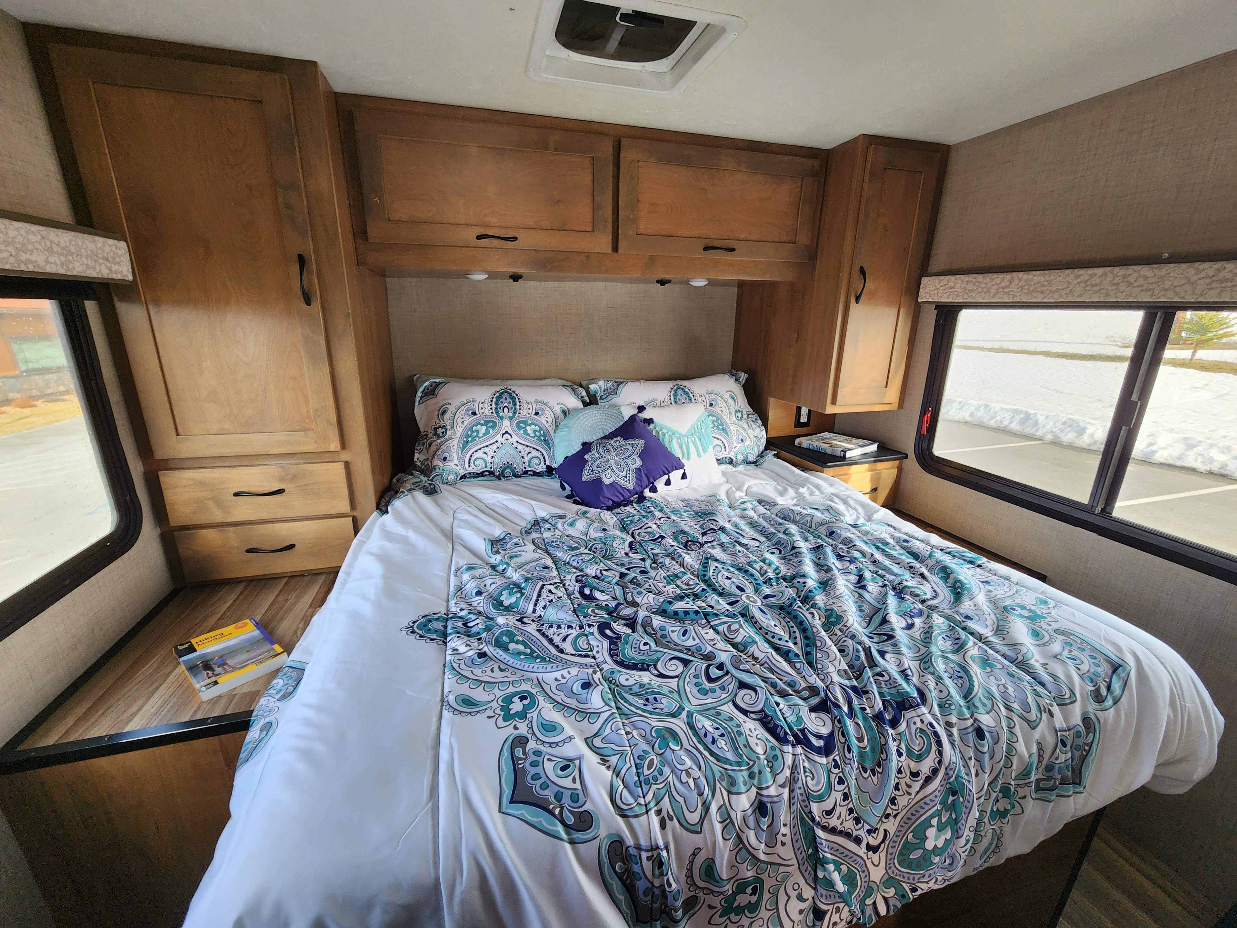 Cozy RV rental bedroom featuring a blue patterned bed, wooden cabinets, and a snowy outdoor view from the window.. Wayfarer Wayfarer Motorhome 2020
