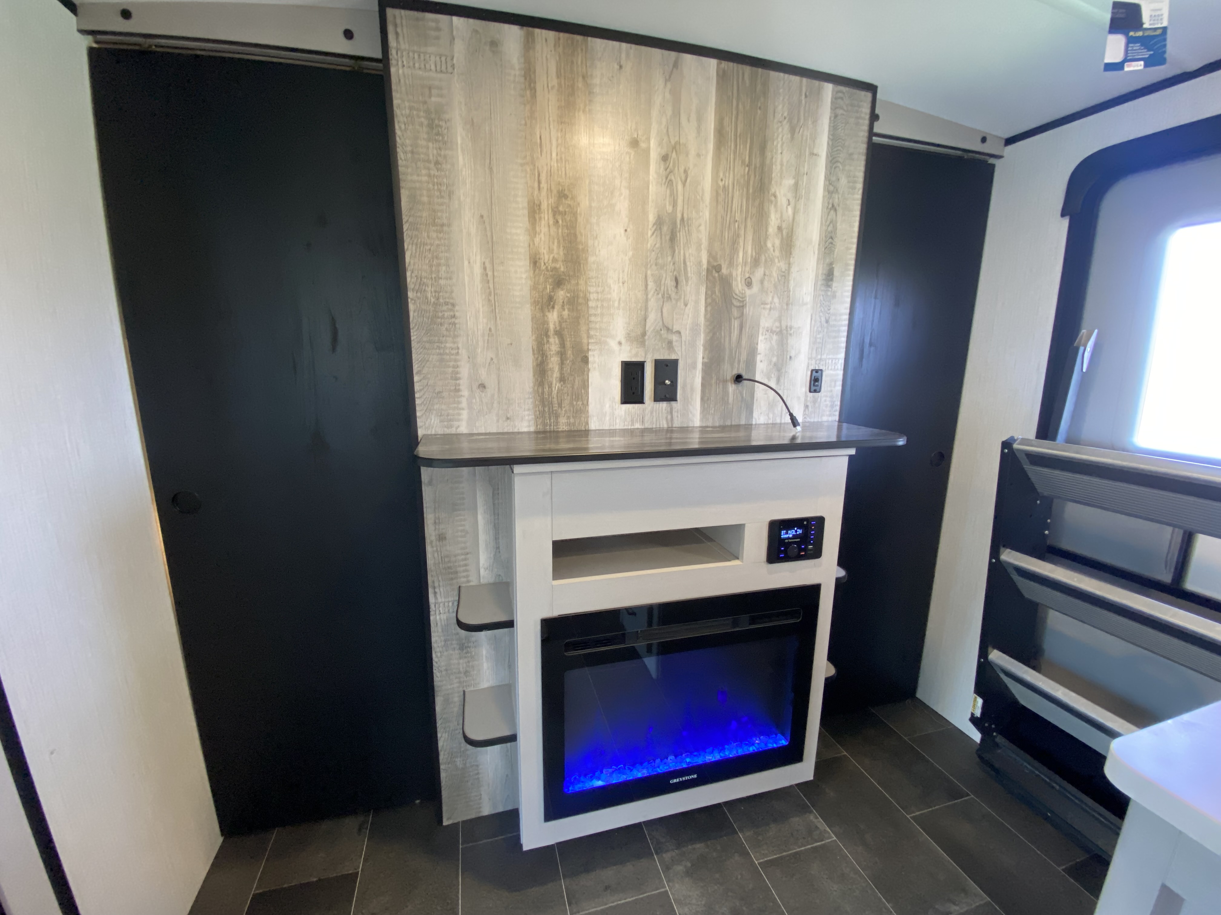 RV rental interior features a modern entertainment unit with a blue electric fireplace, rustic accent wall, and practical sliding doors.. Heartland RVs Mallard 2022