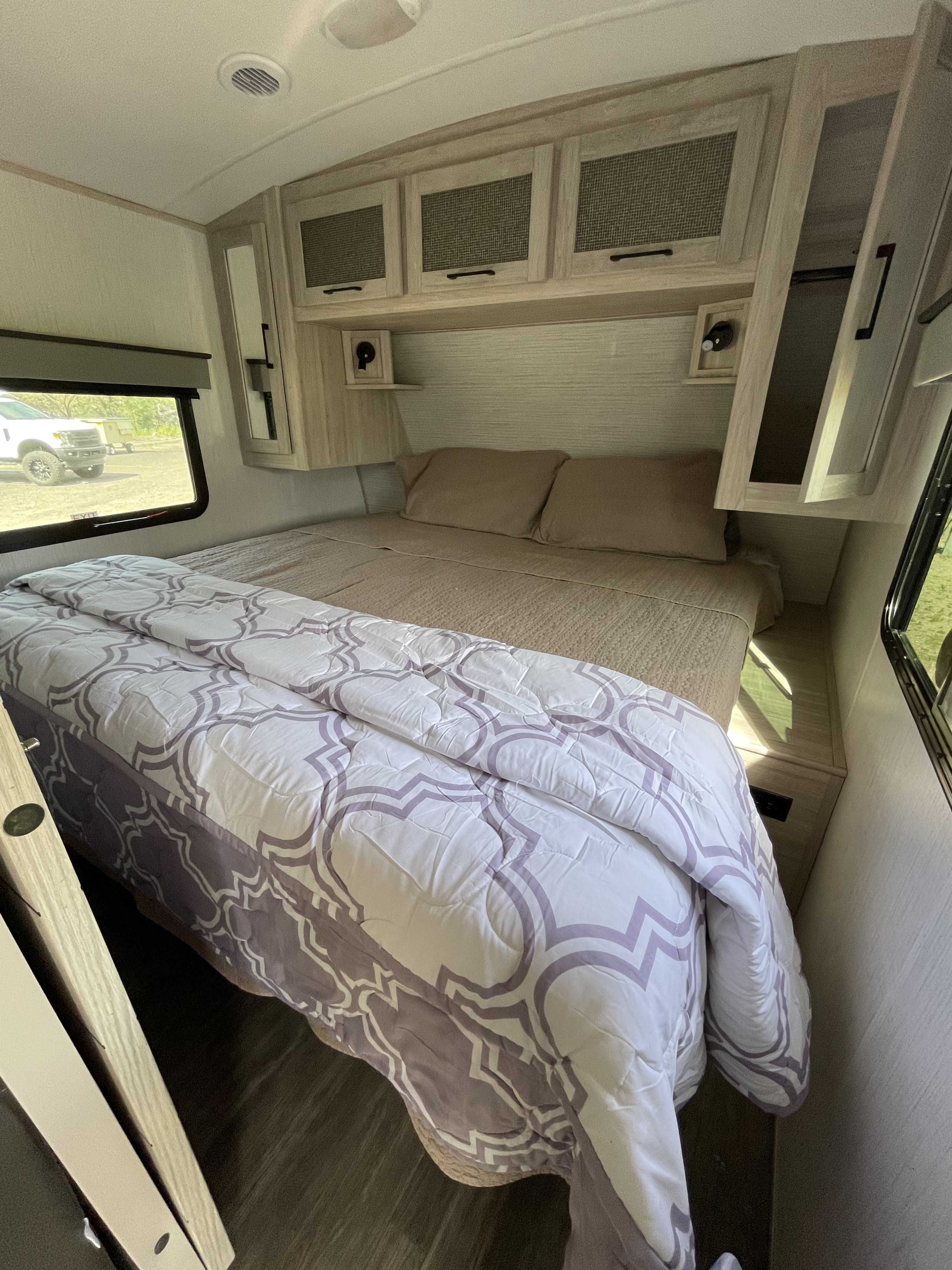 Step into comfort! This RV rental features a cozy bedroom with a patterned bed, ample overhead storage, and natural light.. Twilight RVS Signature 2022