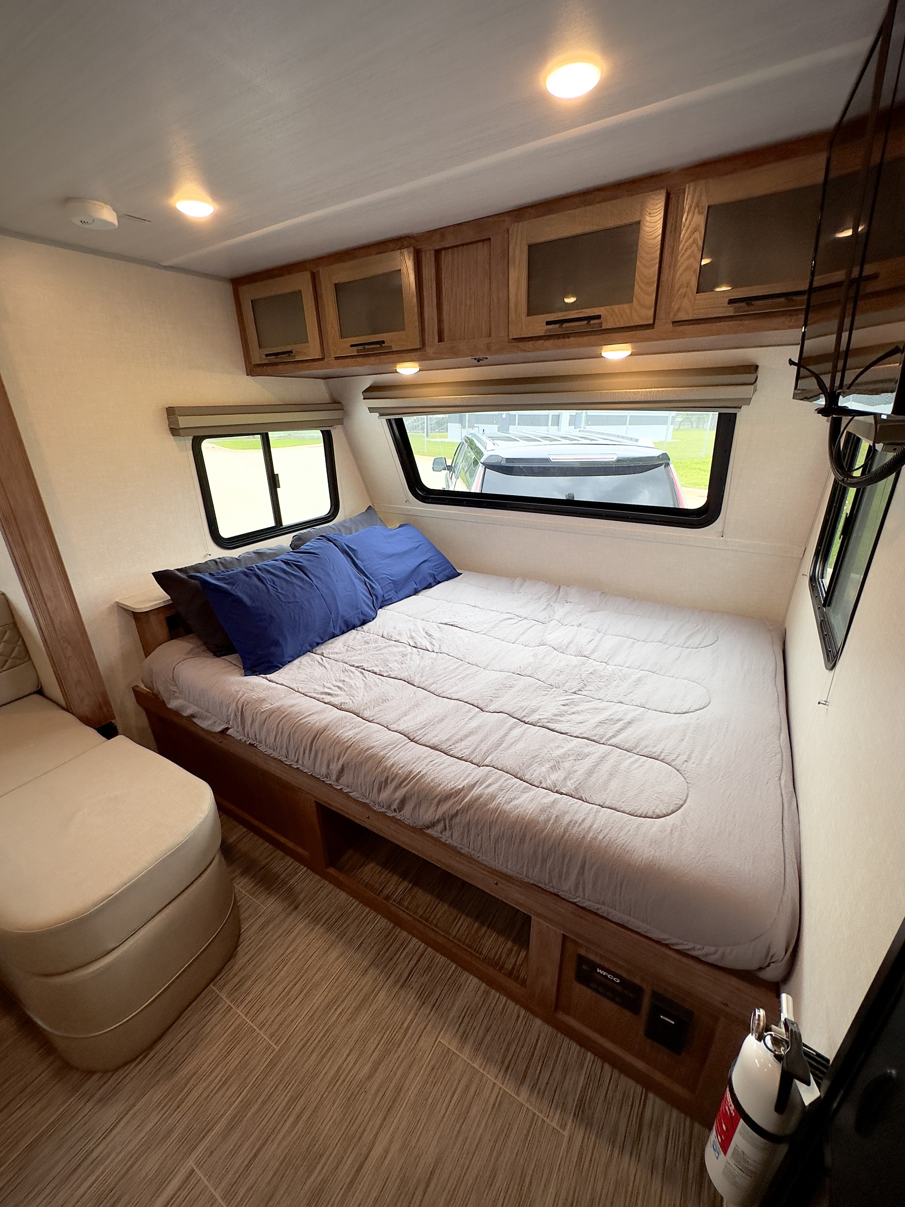 Explore comfort in this RV rental bedroom: bed, blue pillows, overhead cabinets, windows. Under-bed storage & fire extinguisher.. Forest River No Boundaries 2022