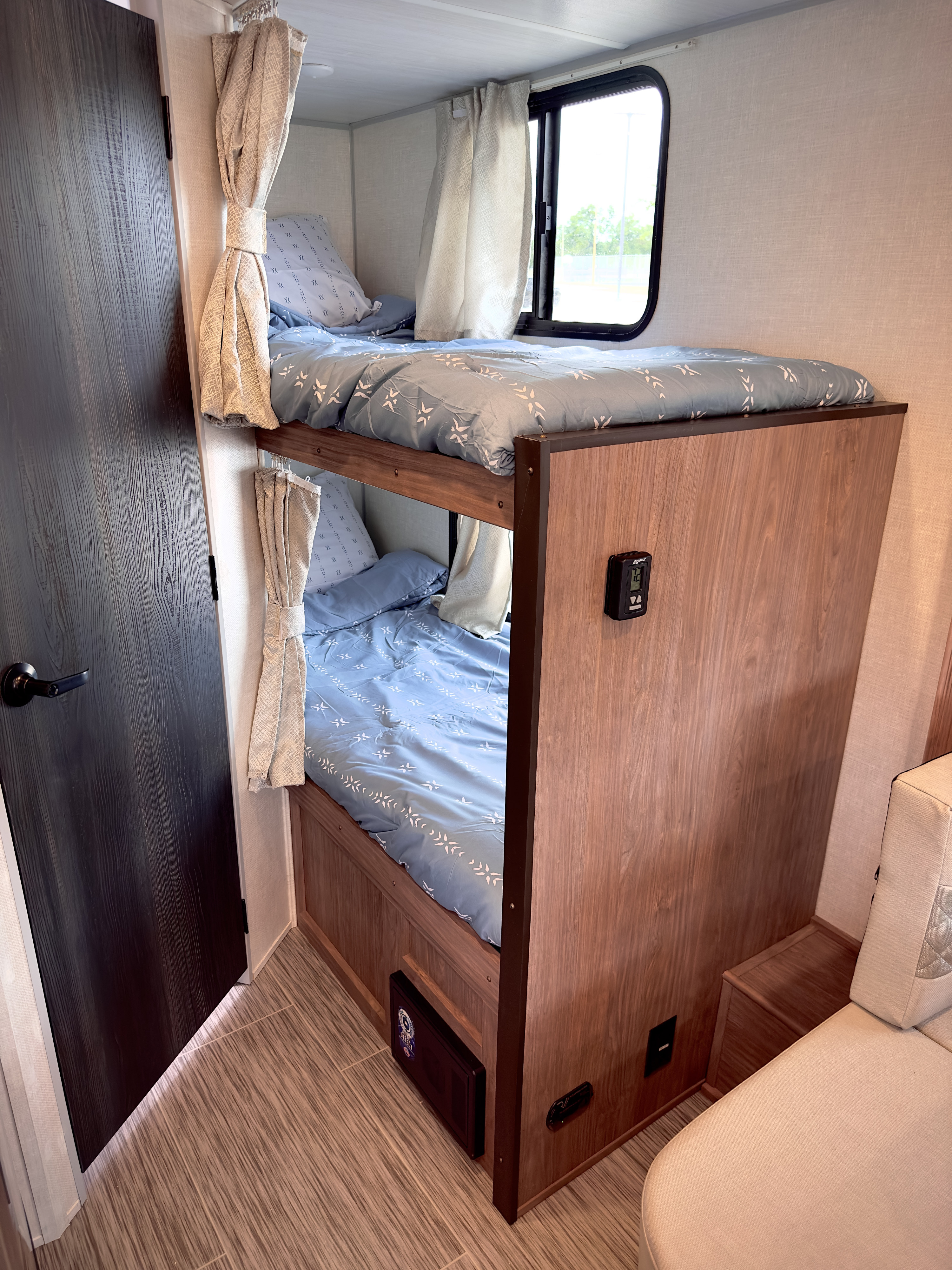 Compact RV rental features bunk beds with blue bedding, curtains, a window, and wood-look flooring.. Forest River No Boundaries 2022