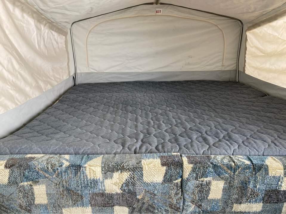 Comfortable pop-up camper bed in an RV rental. Cozy sleeping area with quilted mattress and fabric walls.. Jayco Qwest 2004