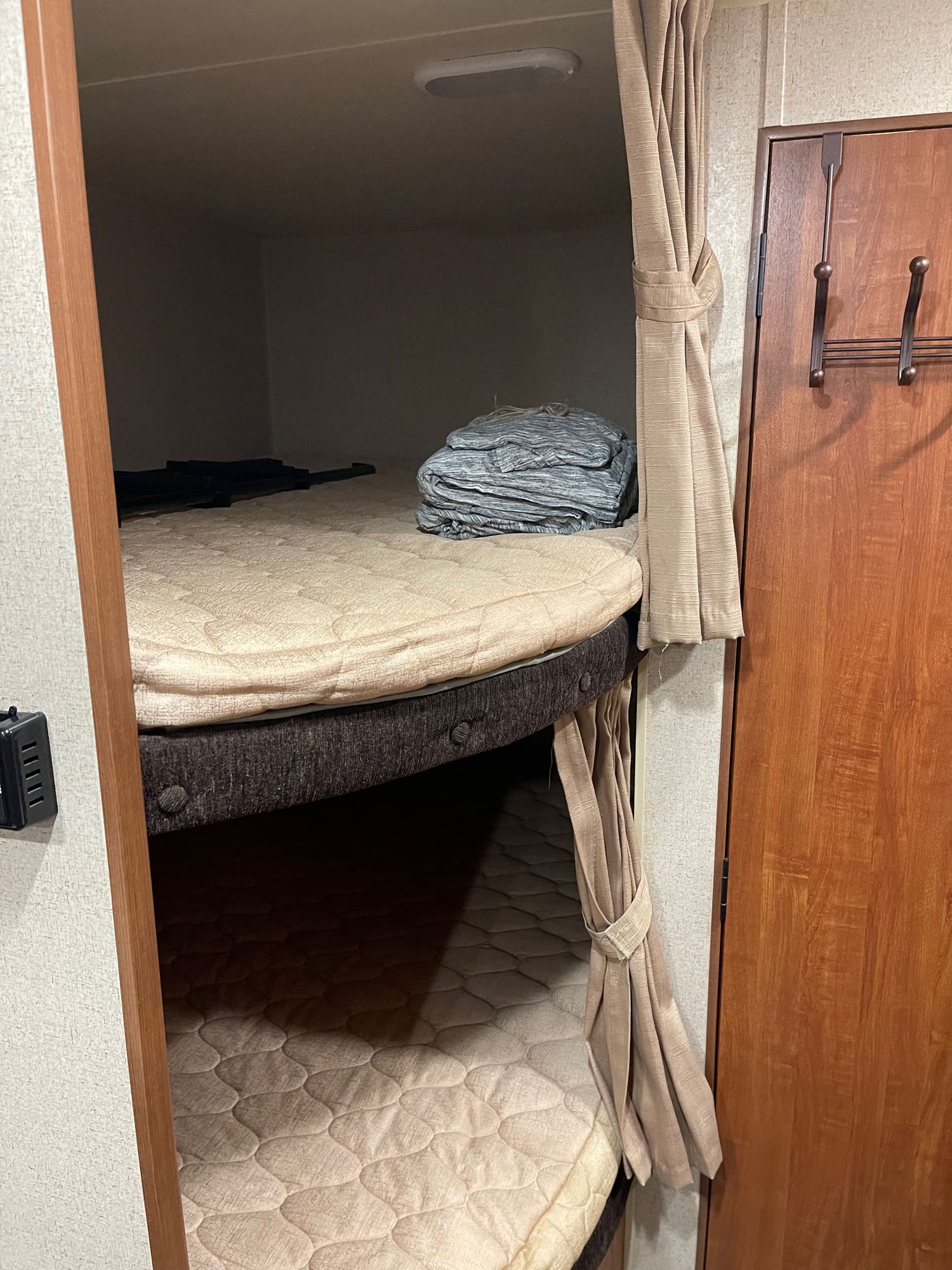 RV rental bunk beds, each with a mattress and side curtains, next to a wood-paneled door with clothes hooks.. Jayco Jay Flight SLX 2018