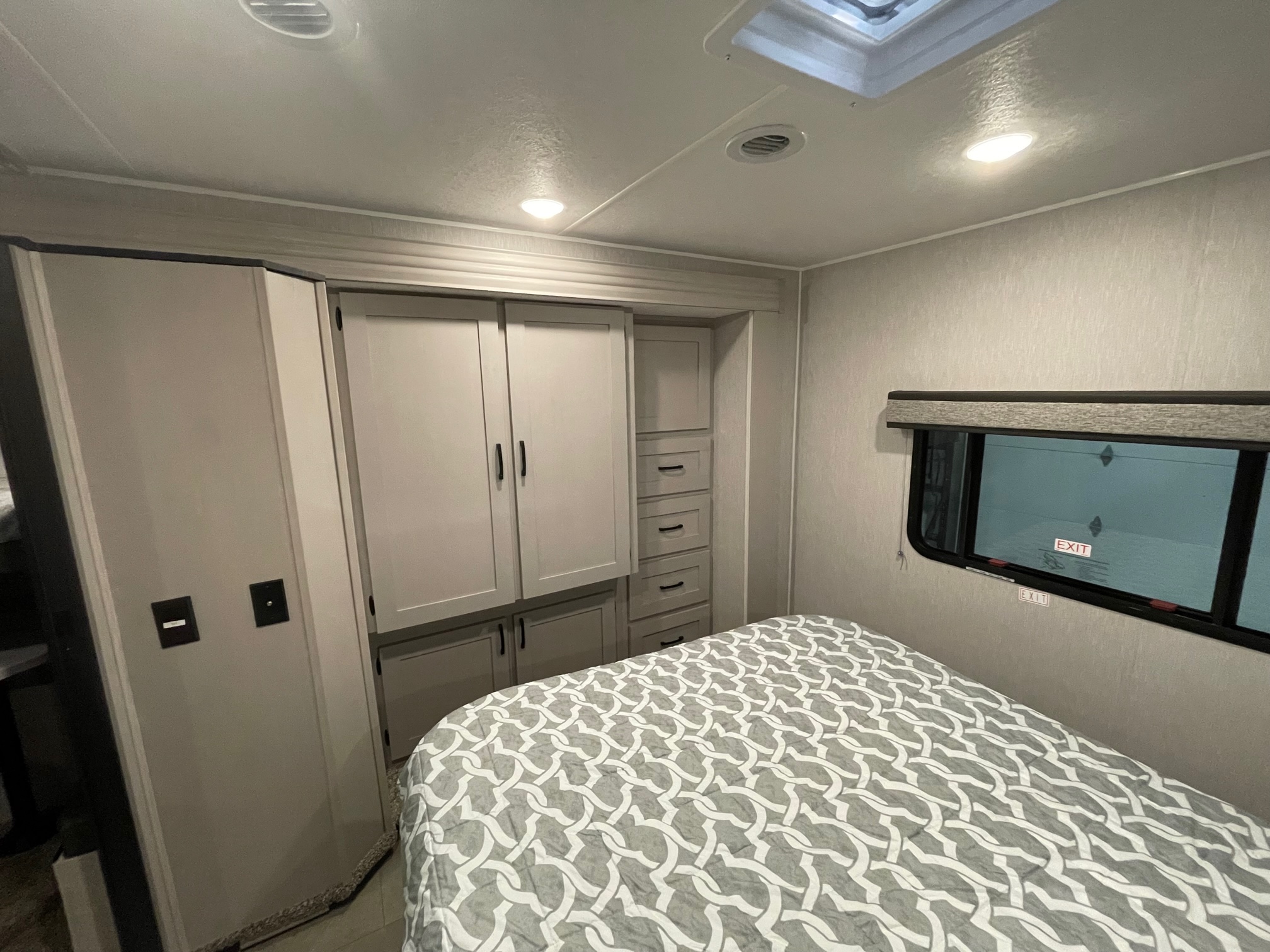 Compact RV rental bedroom featuring a bed with patterned comforter, built-in storage, and emergency exit window.. Coachmen Freelander 2024