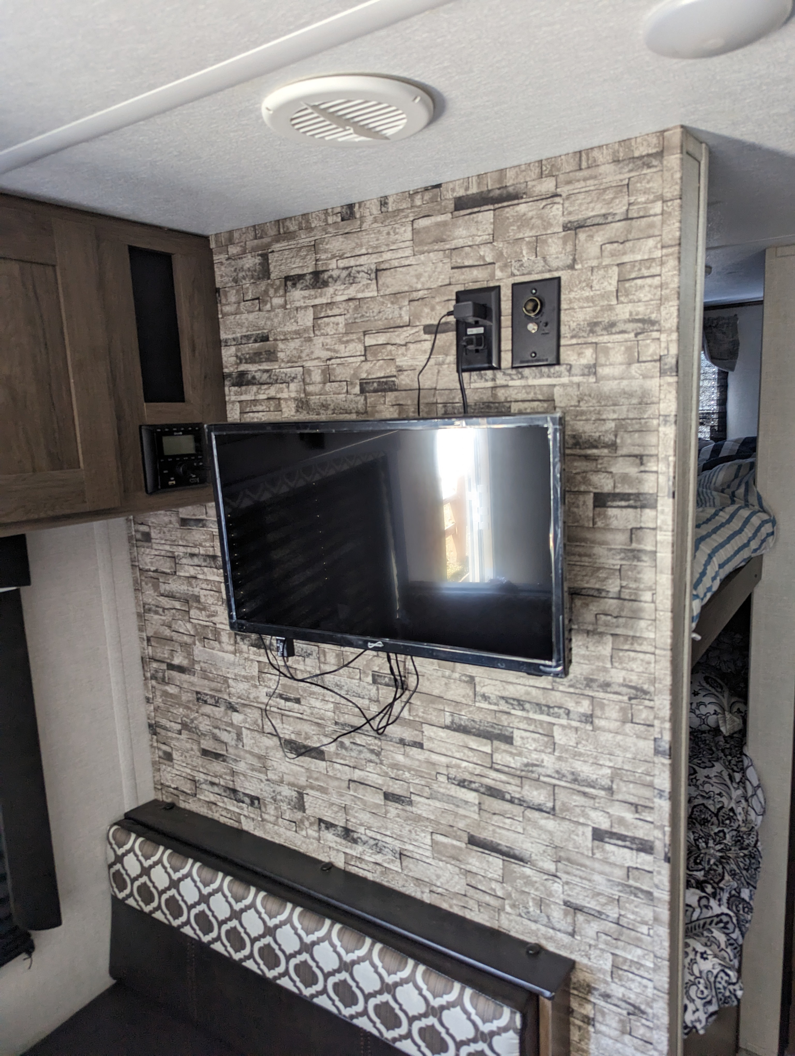 RV rental interior: A mounted TV on a faux stone wall, with an entertainment system, seating, and bunk beds visible.. Avenger 26bk 2021
