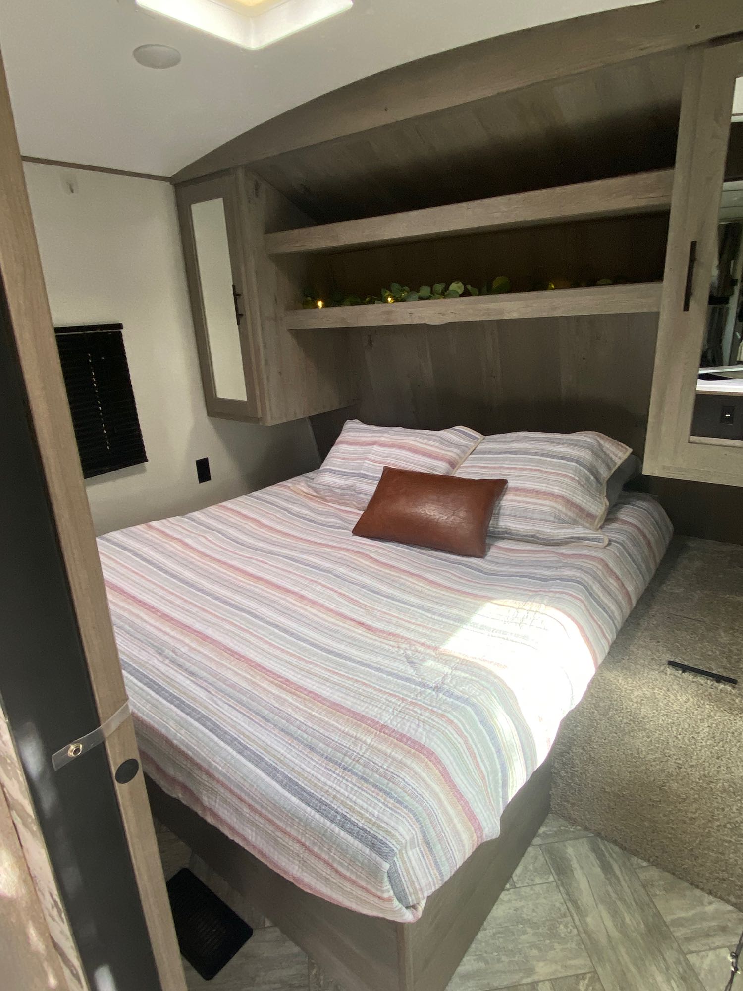 Comfortable RV rental bedroom featuring a striped bed, brown accent pillow, built-in shelving, and a window. Ideal for travelers.. Keystone Springdale 2021