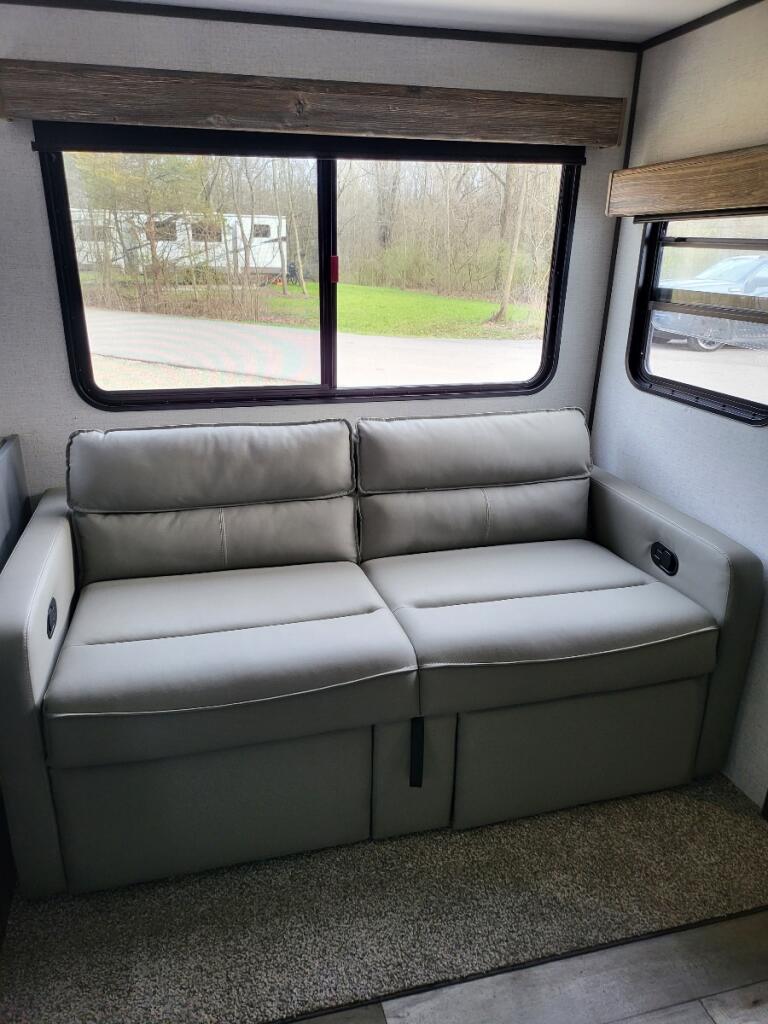 Cozy RV rental interior with a gray sofa and large windows showcasing an outdoor scene with another RV.. Aspen Trail Dutchman 2022