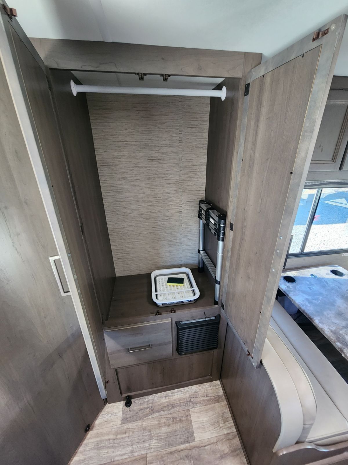 RV rental interior: A functional wardrobe, featuring a hanging rod, shelf with tray, drawer, vent, and collapsible ladder, adjacent to a dinette.. Thor Motor Coach Chateau 2023