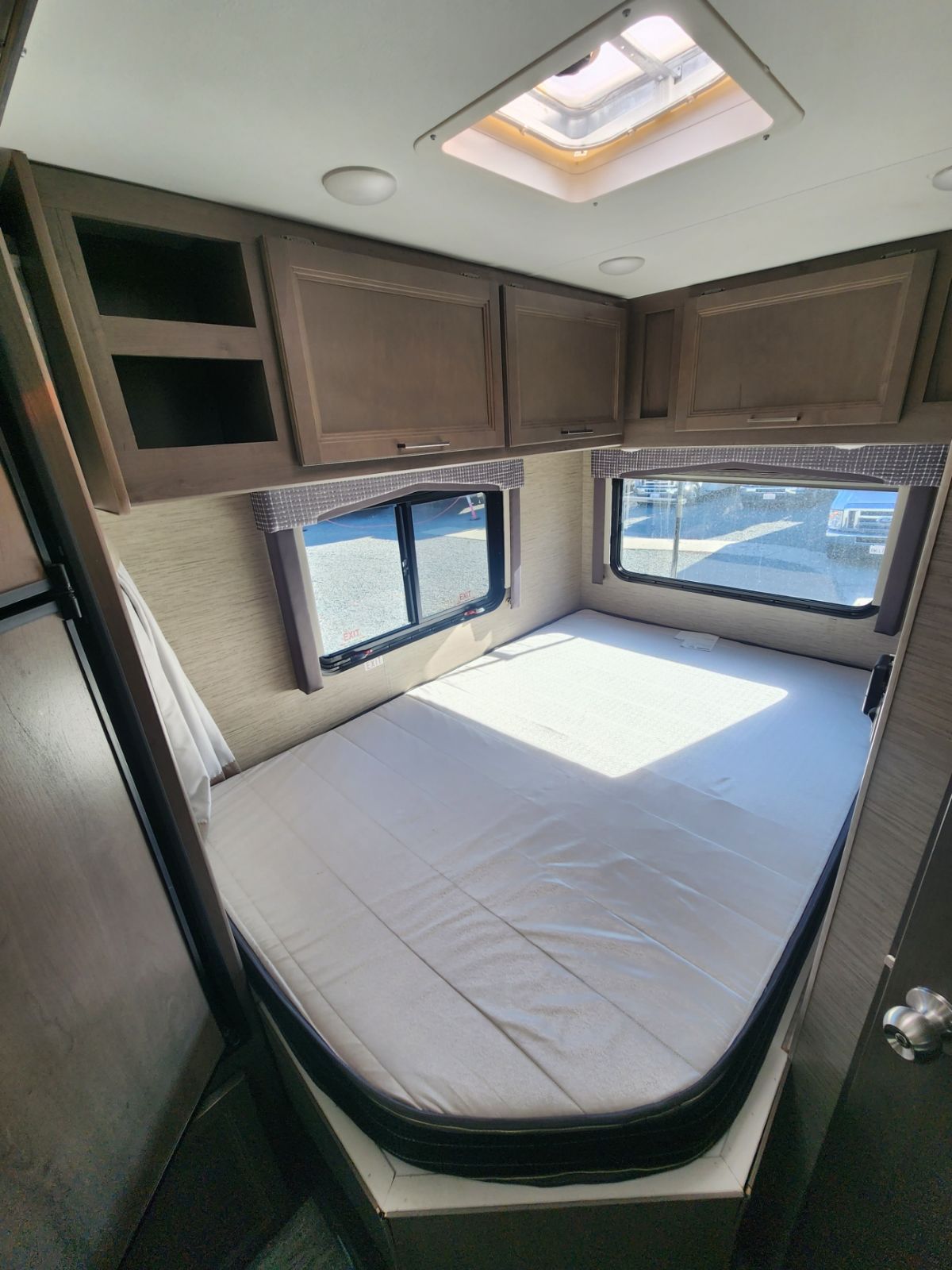 Bright rv rental bedroom featuring a full-sized bed, overhead storage, and windows. A skylight brightens the space for travel.. Thor Motor Coach Chateau 2023