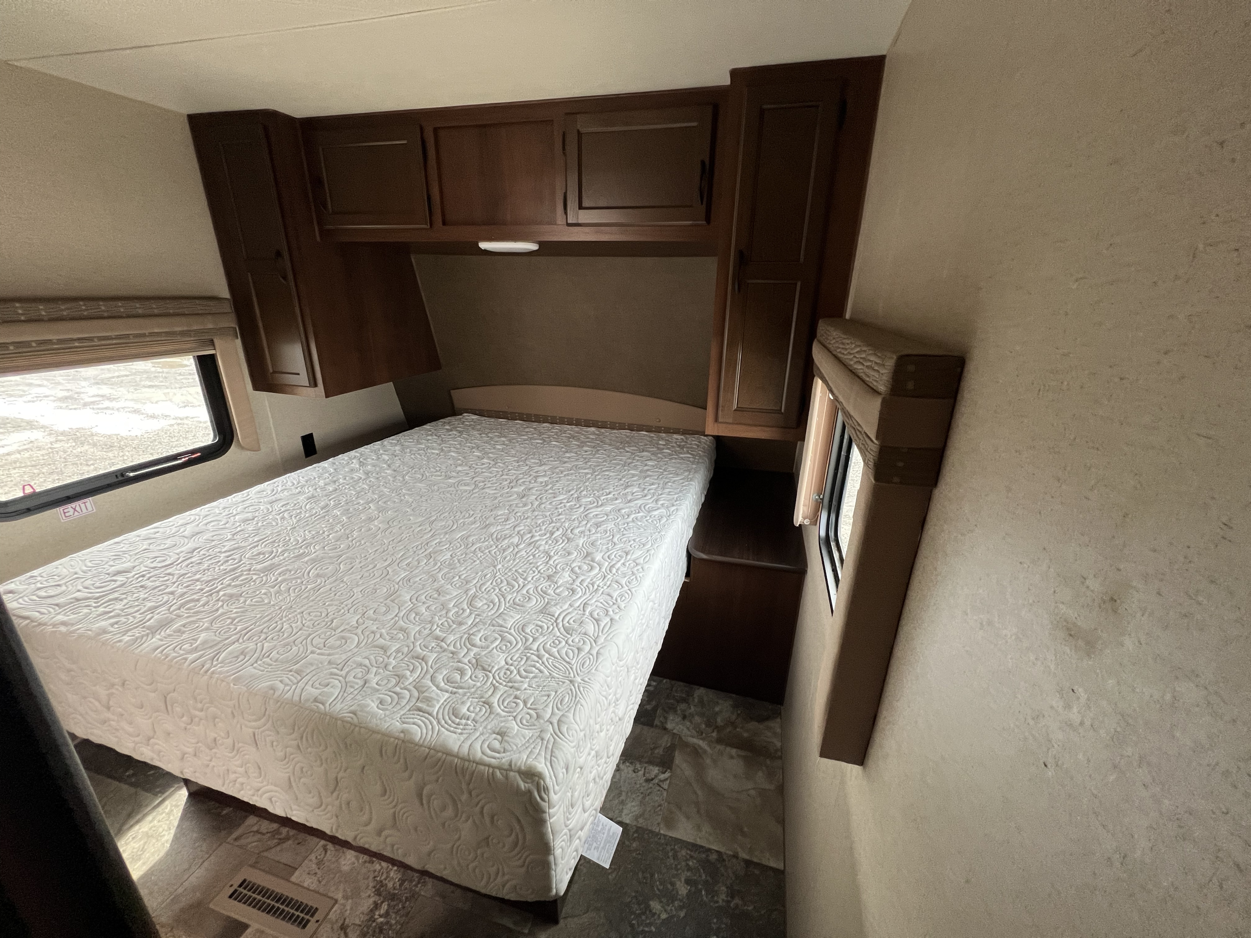 Cozy RV rental bedroom featuring a white quilted bed, dark wood cabinets, and an emergency exit window.. Jayco Jay Flight 2015