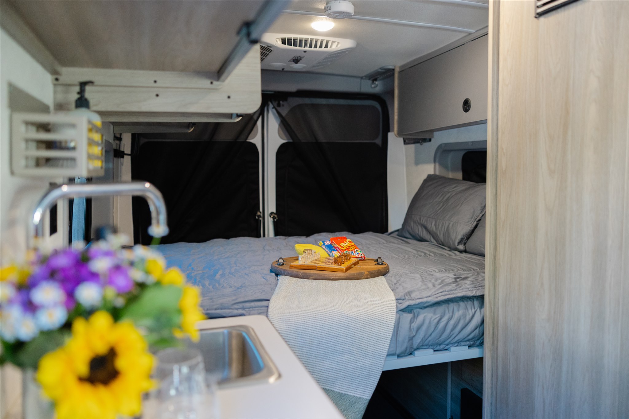 Cozy RV rental interior: bedroom area with chessboard & snacks, plus a compact kitchen. Your road trip starts here!. Winnebago Solis 2022