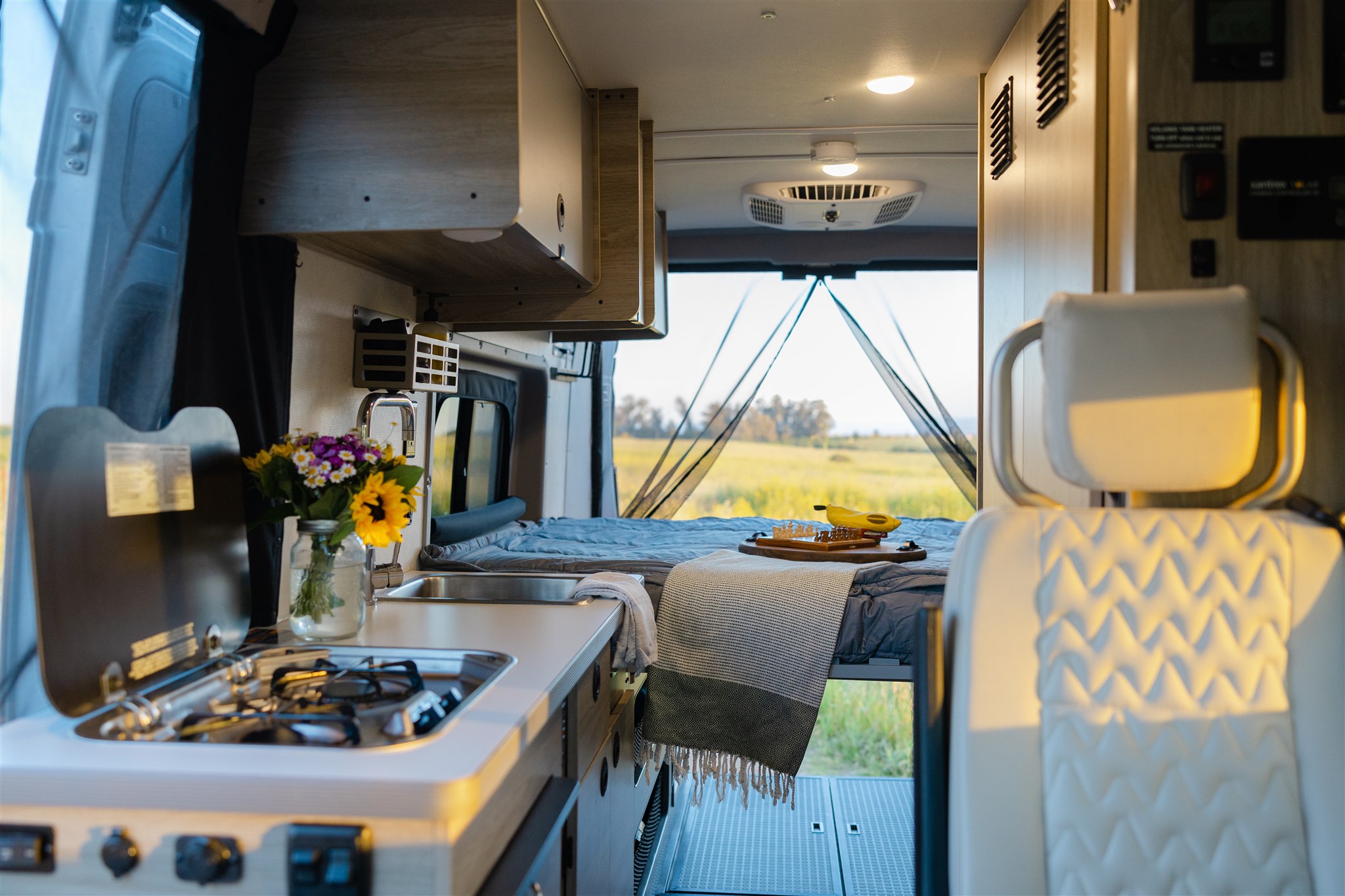 Experience the freedom of an RV rental! This cozy camper van interior features a kitchen, comfortable bed, and scenic outdoor views.. Winnebago Solis 2022