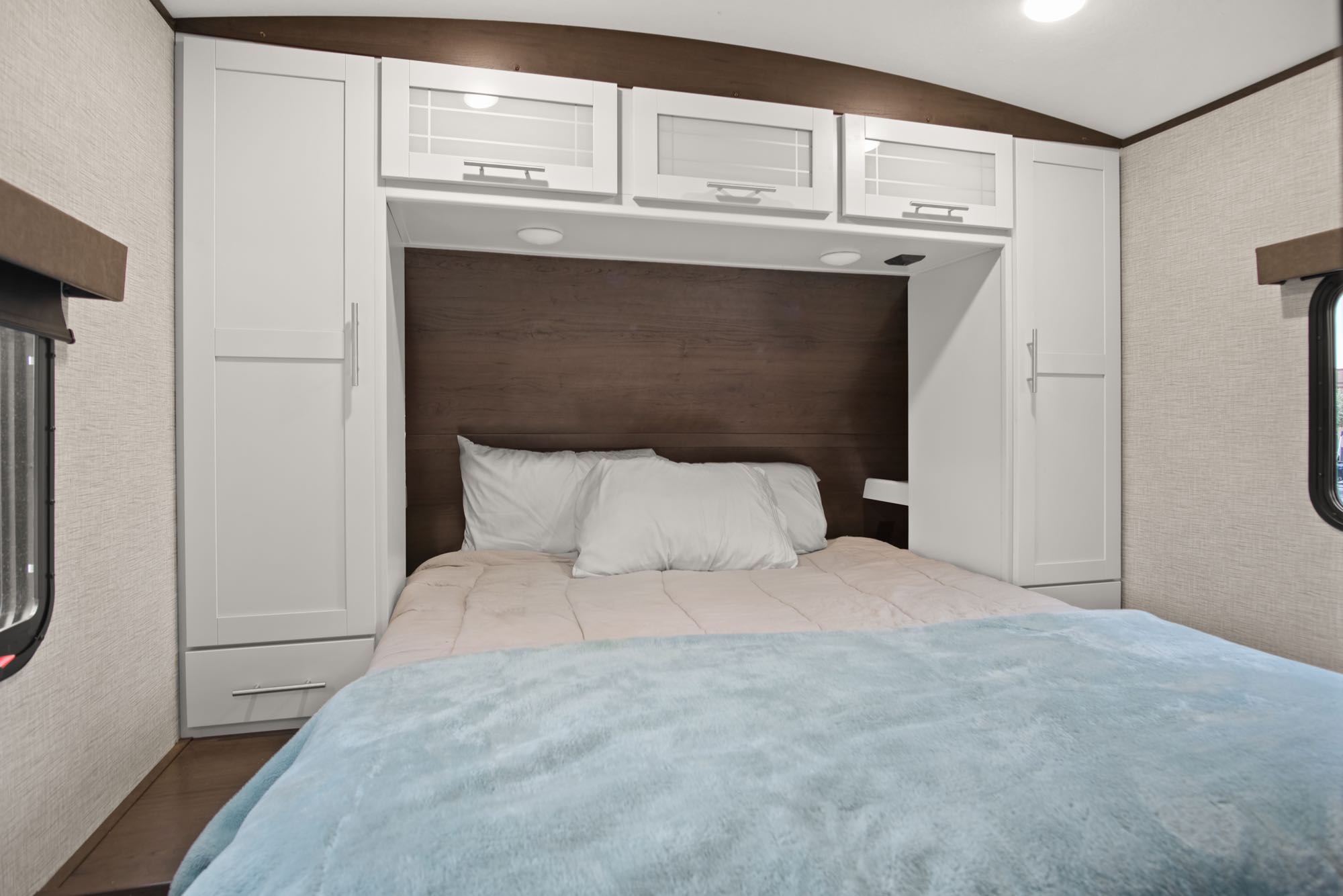 RV rental's inviting bedroom: a comfy bed, wood headboard, and ample white cabinet storage overhead and sides.. Keystone RV Bullet Premier Ultra 2021