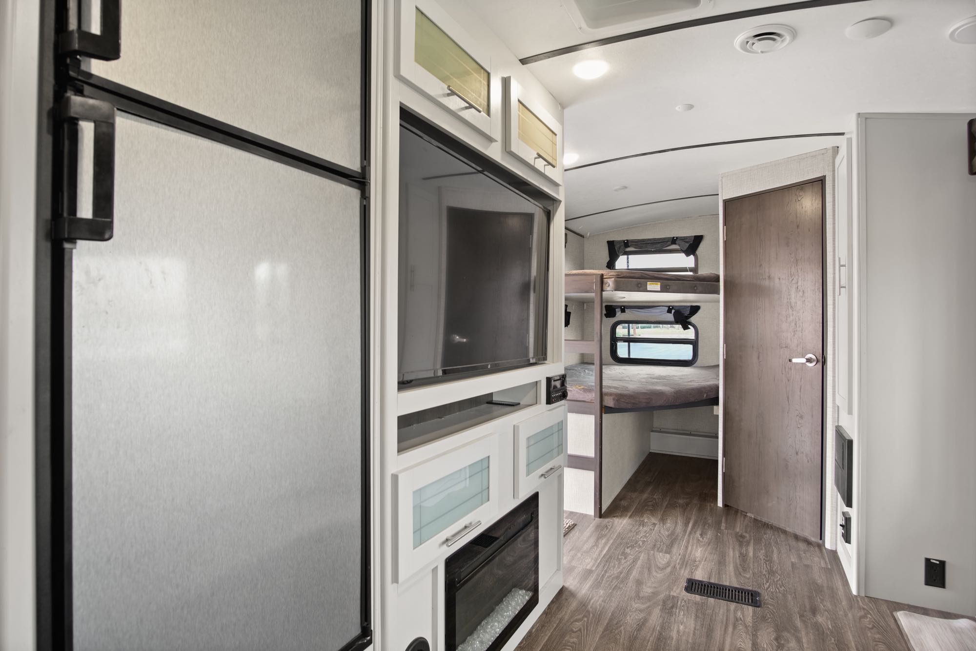 Inside this RV rental: a compact living area with a large fridge, entertainment center, fireplace, and bunk room access.. Keystone RV Bullet Premier Ultra 2021