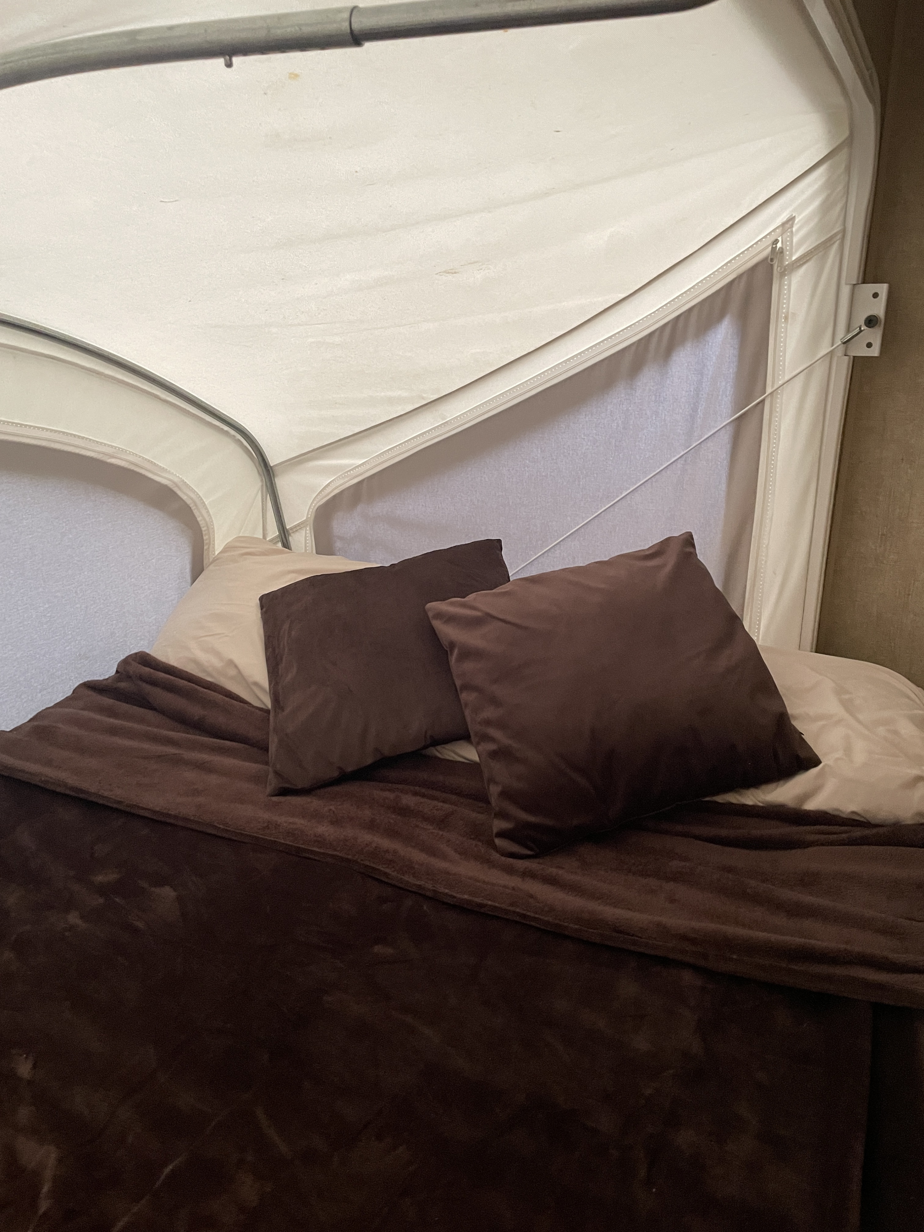 Cozy bed setup in an RV rental, featuring brown pillows and a warm blanket for a comfortable sleep.. Coachmen Classic 2015