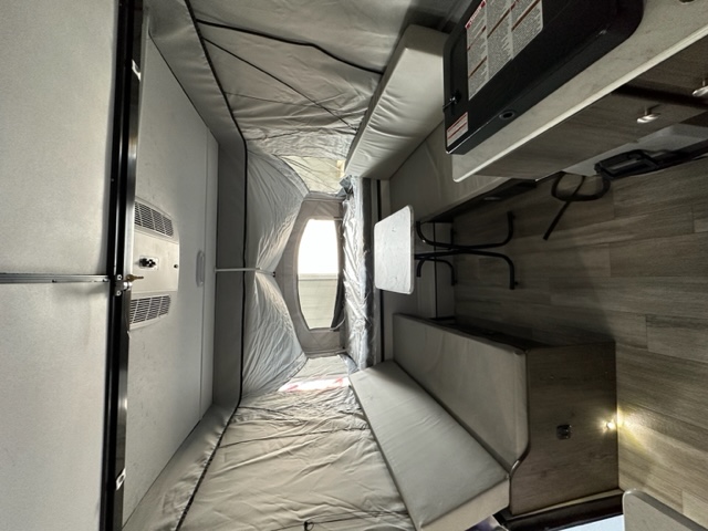 RV rental interior: bed/seating, pop-out tent extension, wood-look floor, small dining table, and kitchen with stove.. Coachmen Clipper 806XLS 2022