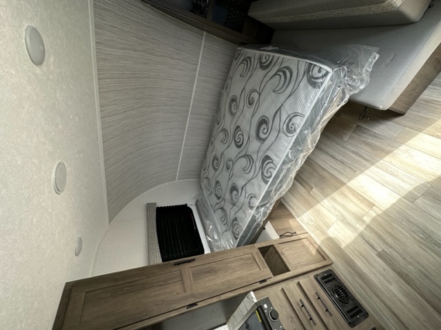 Inside a modern RV rental: New mattress in plastic, light-toned walls with a curved ceiling, wood-look floor, & compact cabinets.. Coachmen Clipper 182DBU 2022
