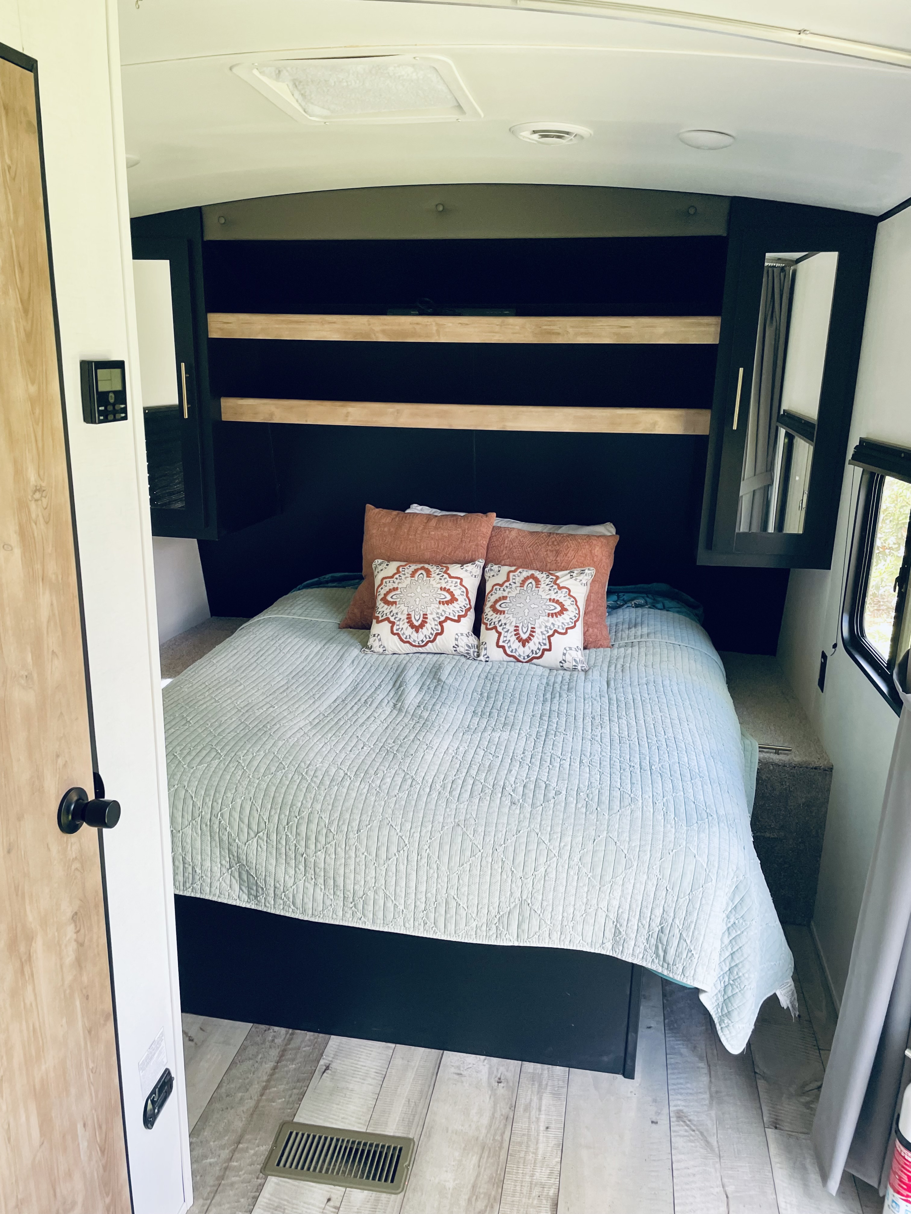 An RV rental's cozy bedroom, showcasing a bed with light blue quilt, accent pillows, dark built-in storage, and wood flooring.. Keystone RV Springdale 2022