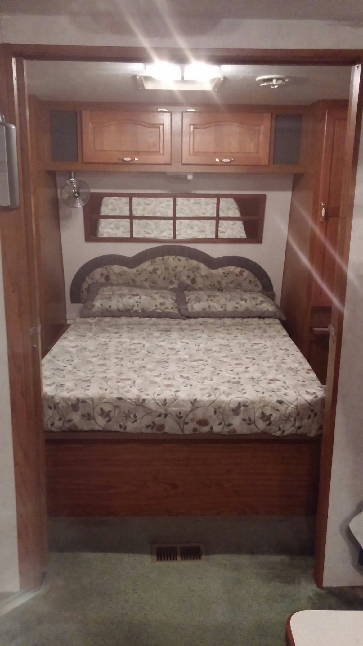 Compact RV rental bedroom with a floral bed, wood cabinets, and an overhead fan, showing a cozy sleeping space.. Chateau Chateau Trailer 2001